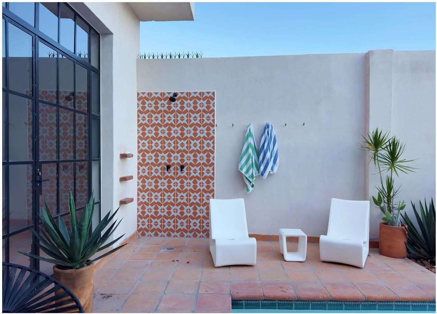 White sculptural outdoor chairs beside a patterned wall and tall window