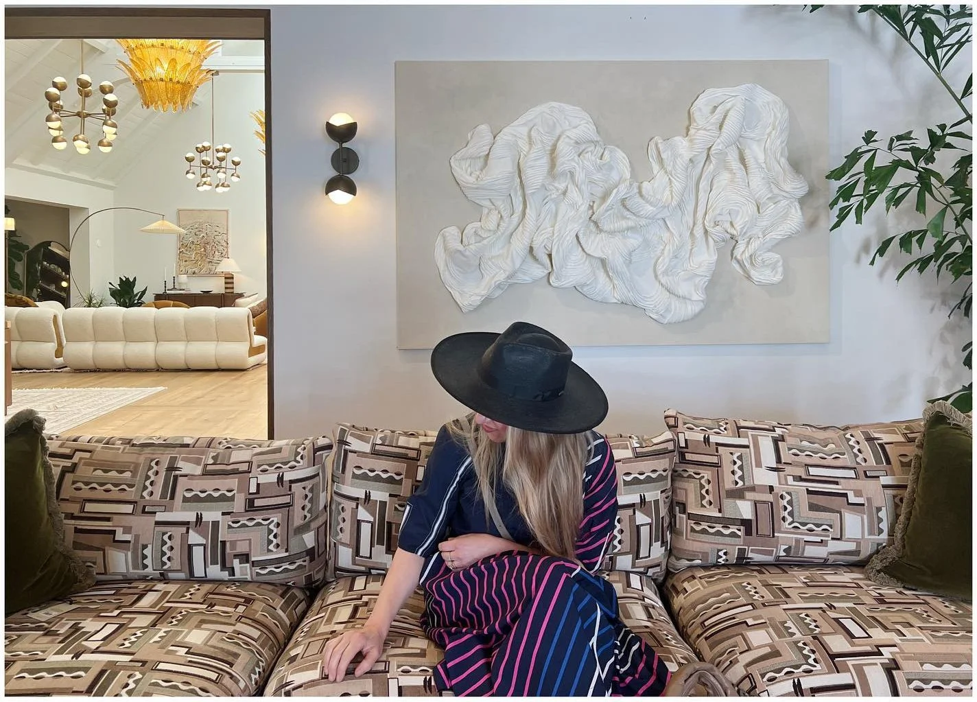 Designer seated on a patterned sofa beneath sculptural wall art in a showroom