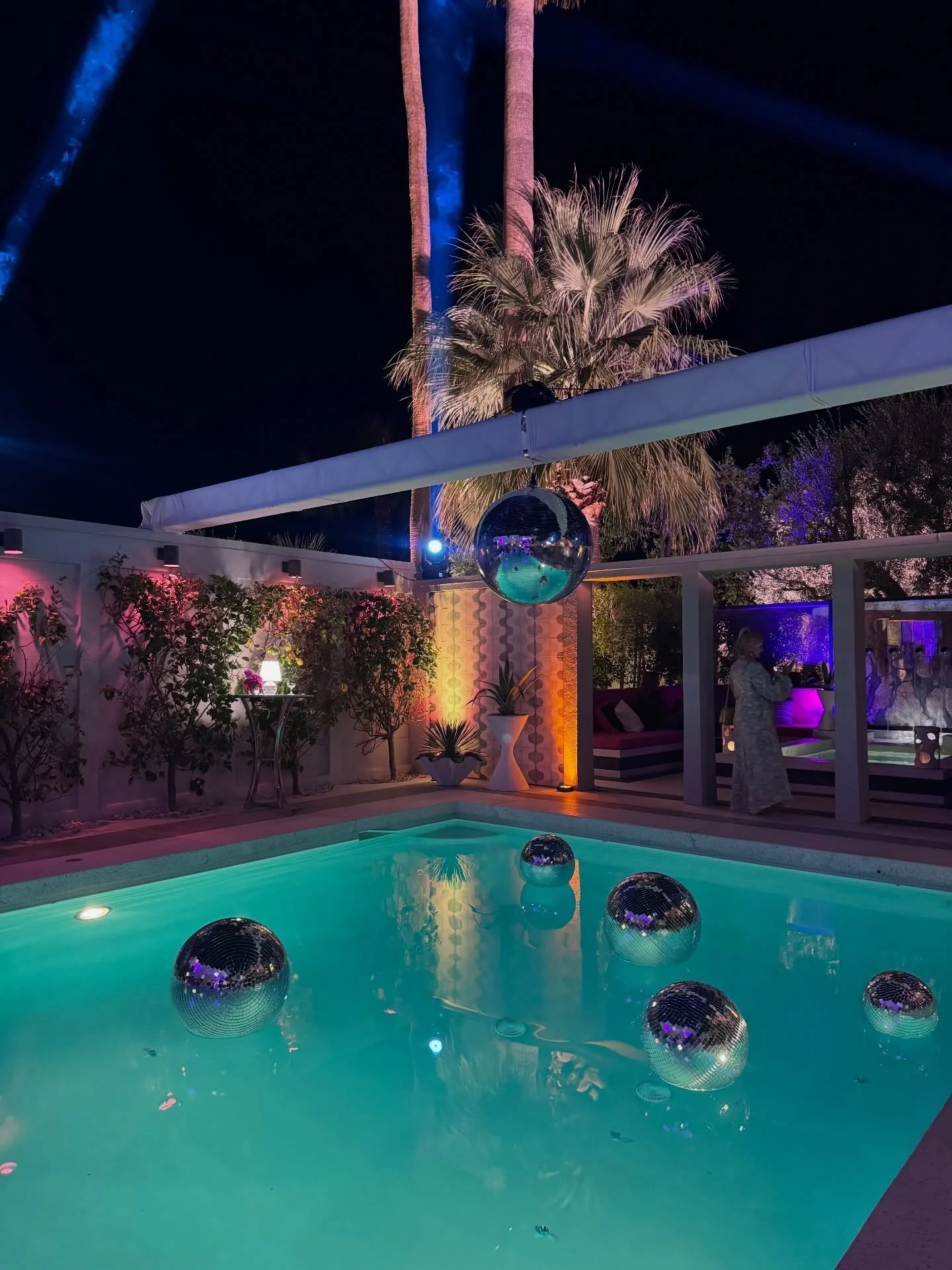 Nighttime pool reflecting palms and colored event lights