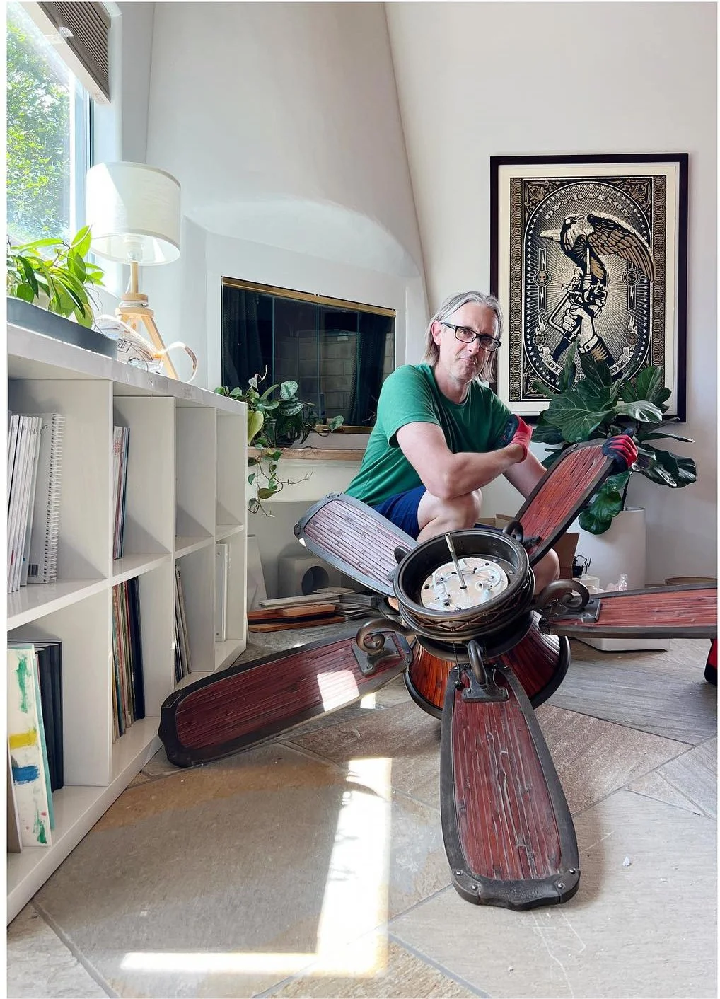 Person holding a large ceiling fan in a bright room with built-in shelving.