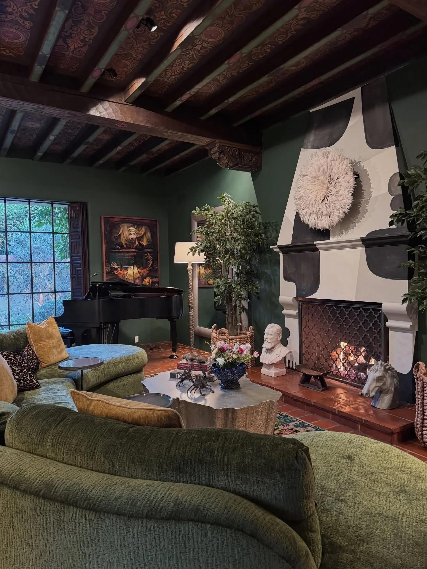 Green sofas beneath exposed beams beside a carved fireplace