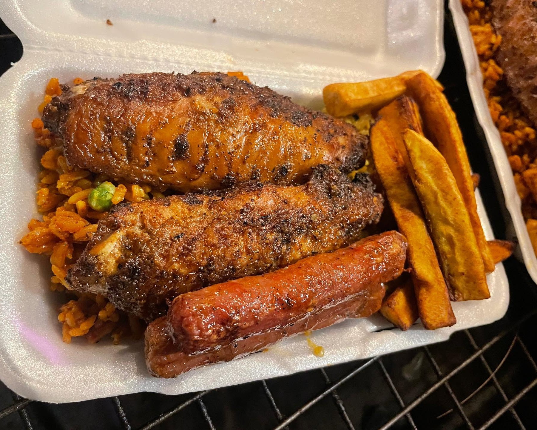 Takeout meal with grilled chicken, sausage, seasoned rice, and golden fries in a foam container