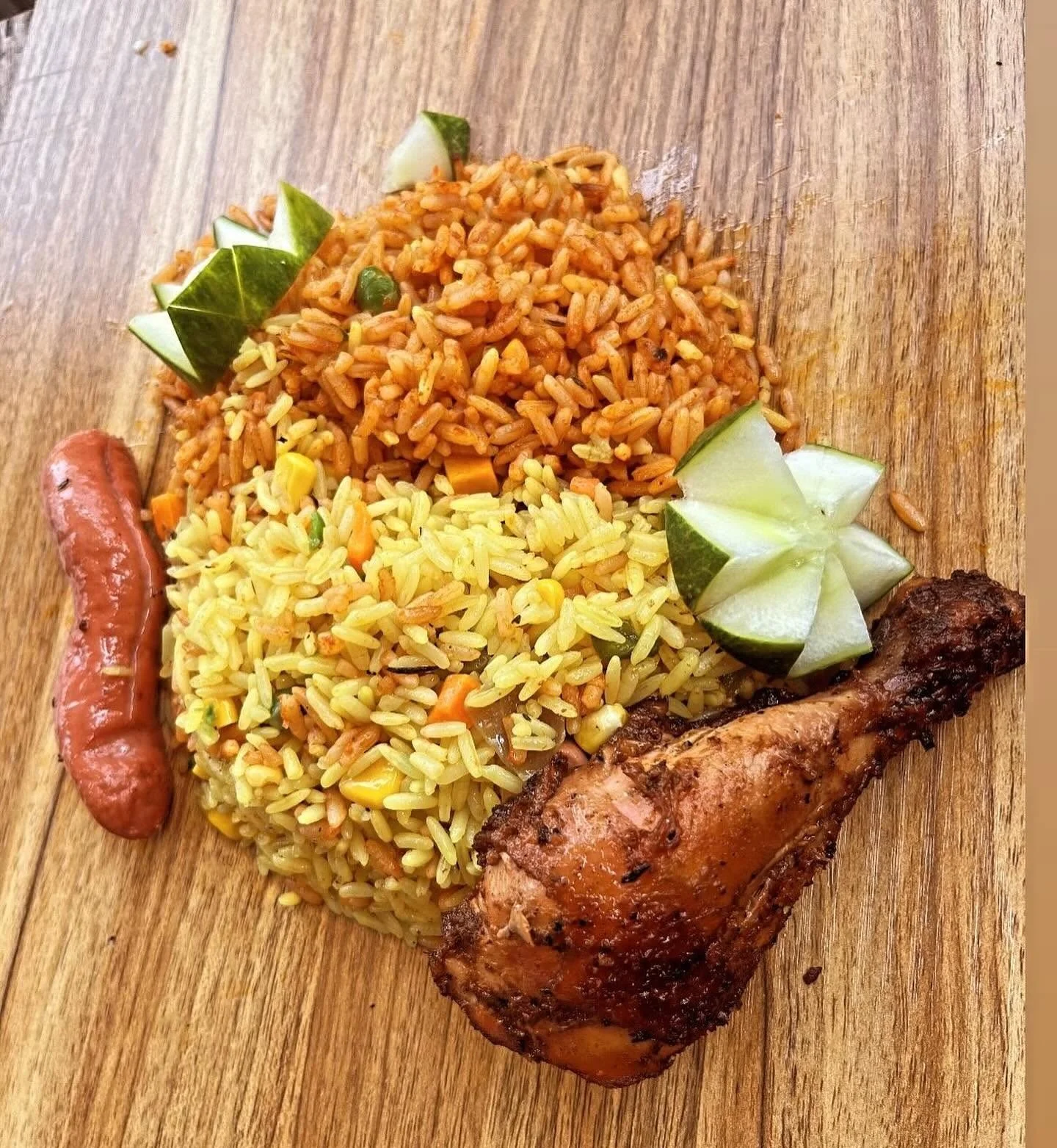 Plate of seasoned yellow and orange rice with grilled chicken, sausage, cucumber garnishes, and vegetables on a wooden table