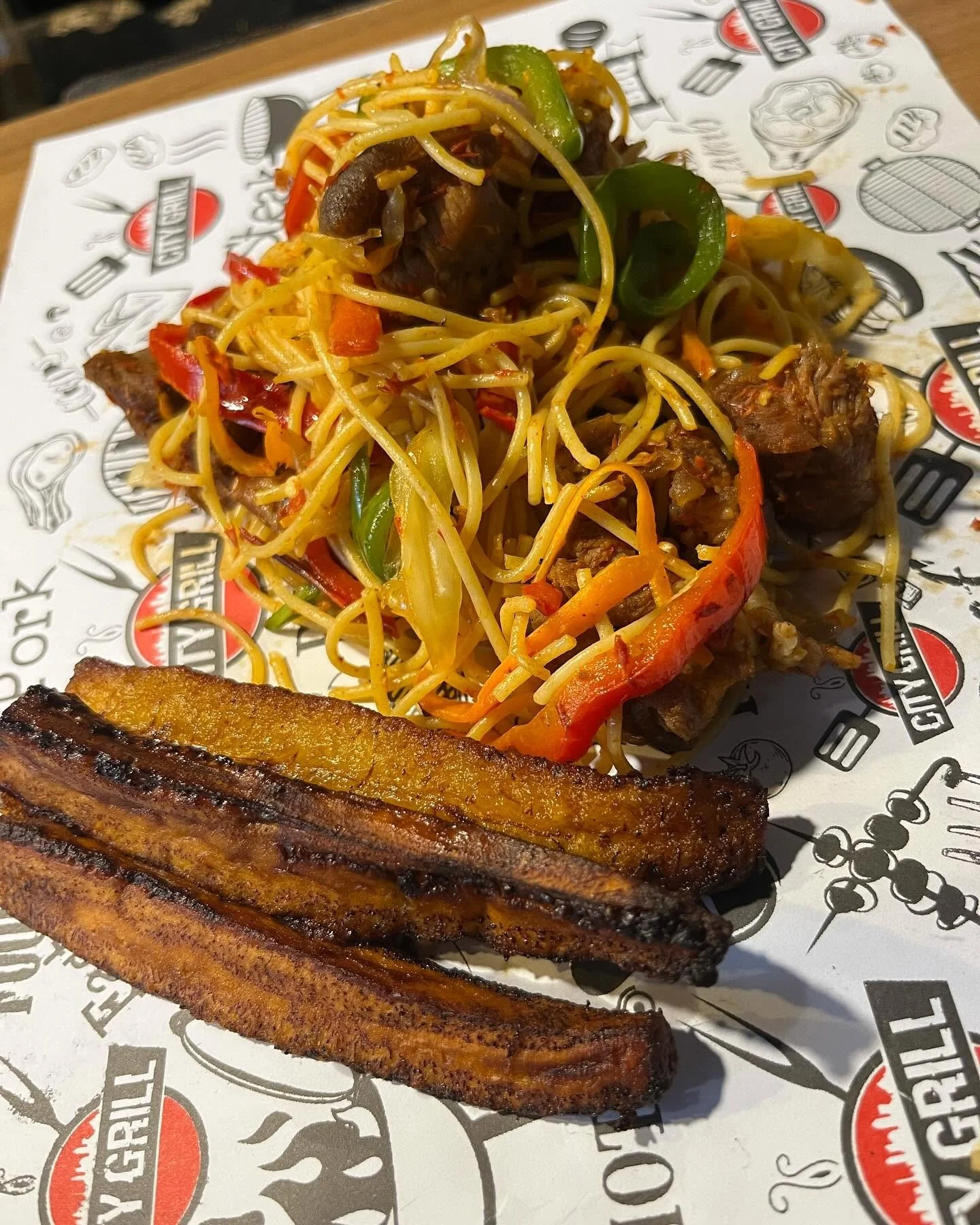 Grilled beef ribs with stir-fried noodles, peppers, onions, and carrots on a restaurant plate
