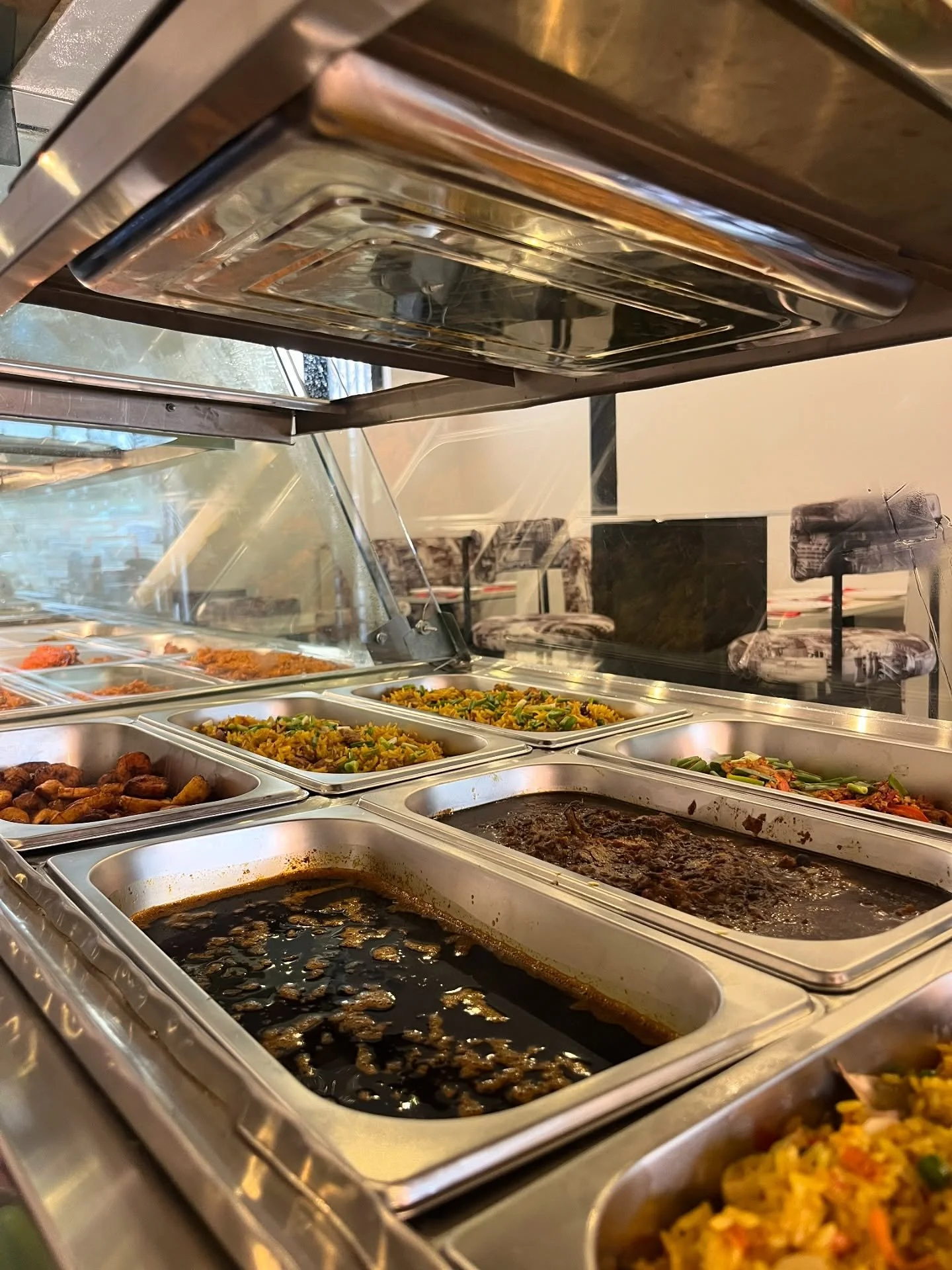 Buffet serving station with trays of seasoned rice, vegetables, fried plantains, and saucy meat dishes
