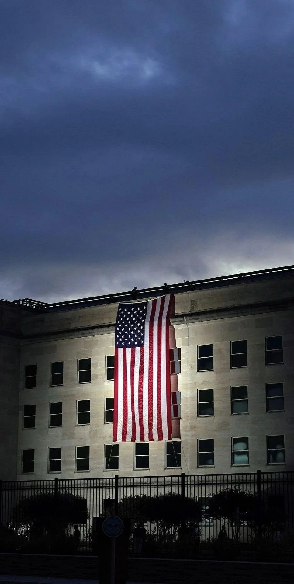 Large American flag displayed on a building facade beneath a dark, cloudy evening sky