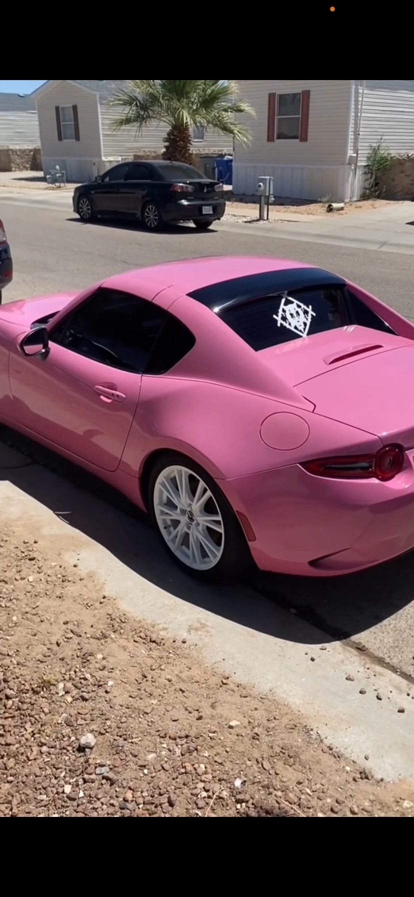 Bright pink sports coupe with tinted windows and white custom wheels parked beside a manufactured home.