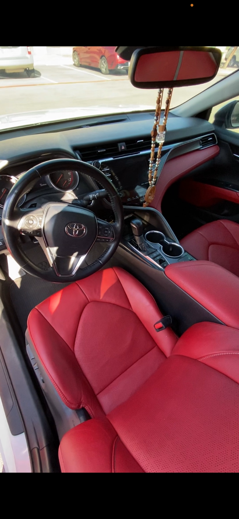 Detailed Toyota sedan interior with red leather seats, black dashboard, steering wheel, center console, and hanging beaded ornament