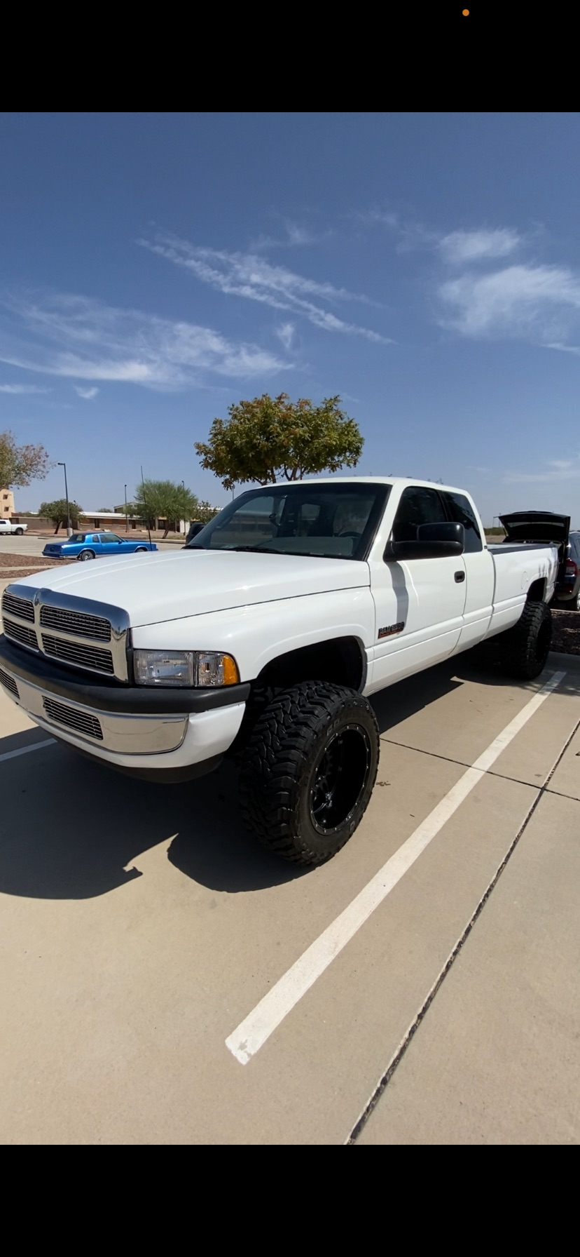 Detailed Lifted white Dodge Ram pickup truck with oversized off-road tires parked in a sunny parking lot