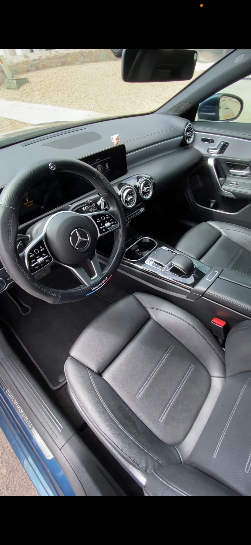 Interior of a modern Mercedes-Benz vehicle with black leather seats, multifunction steering wheel, dashboard display, circular air vents, and center console.