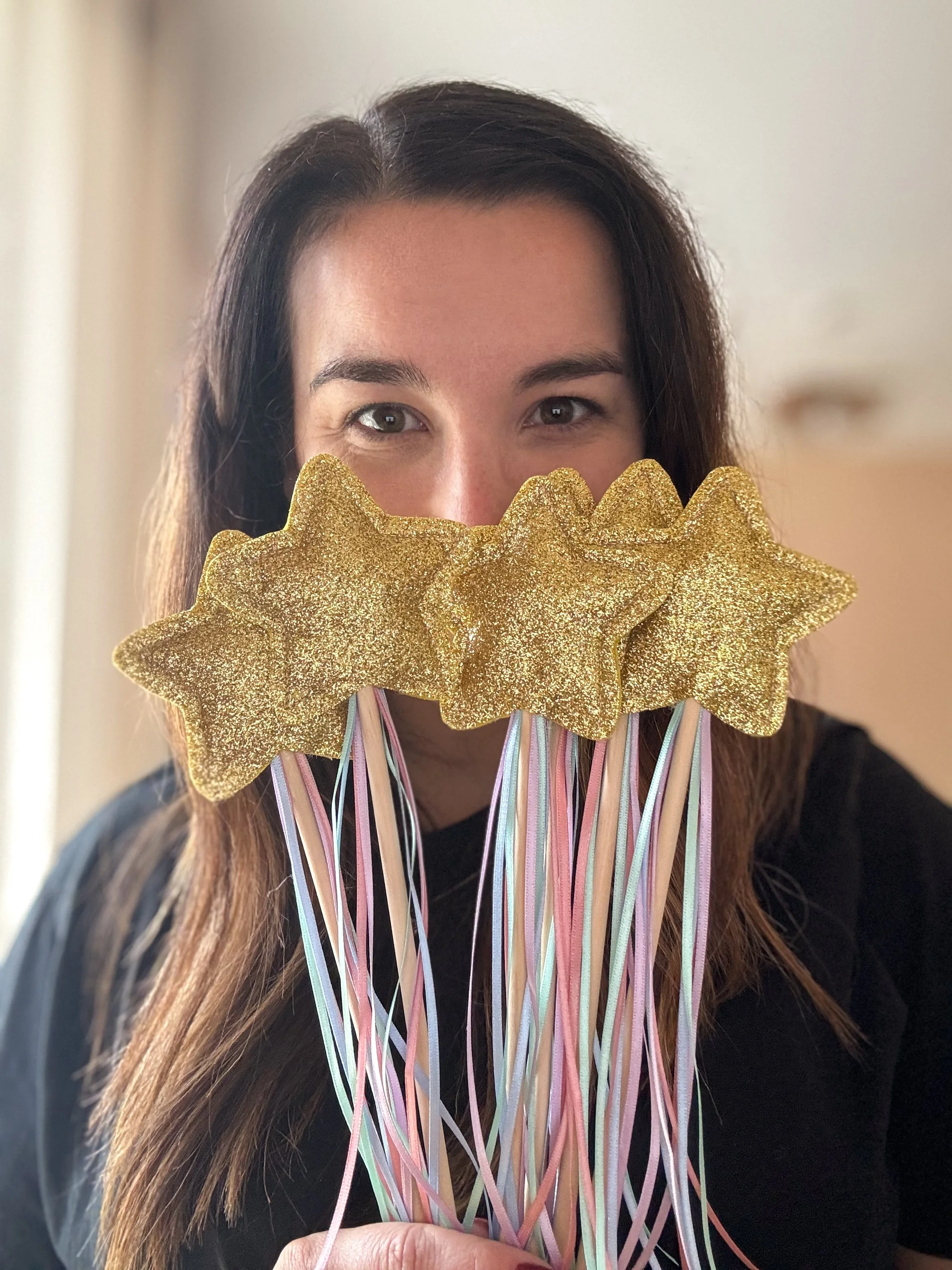 Woman holding a large glittery gold flower with pastel ribbon streamers