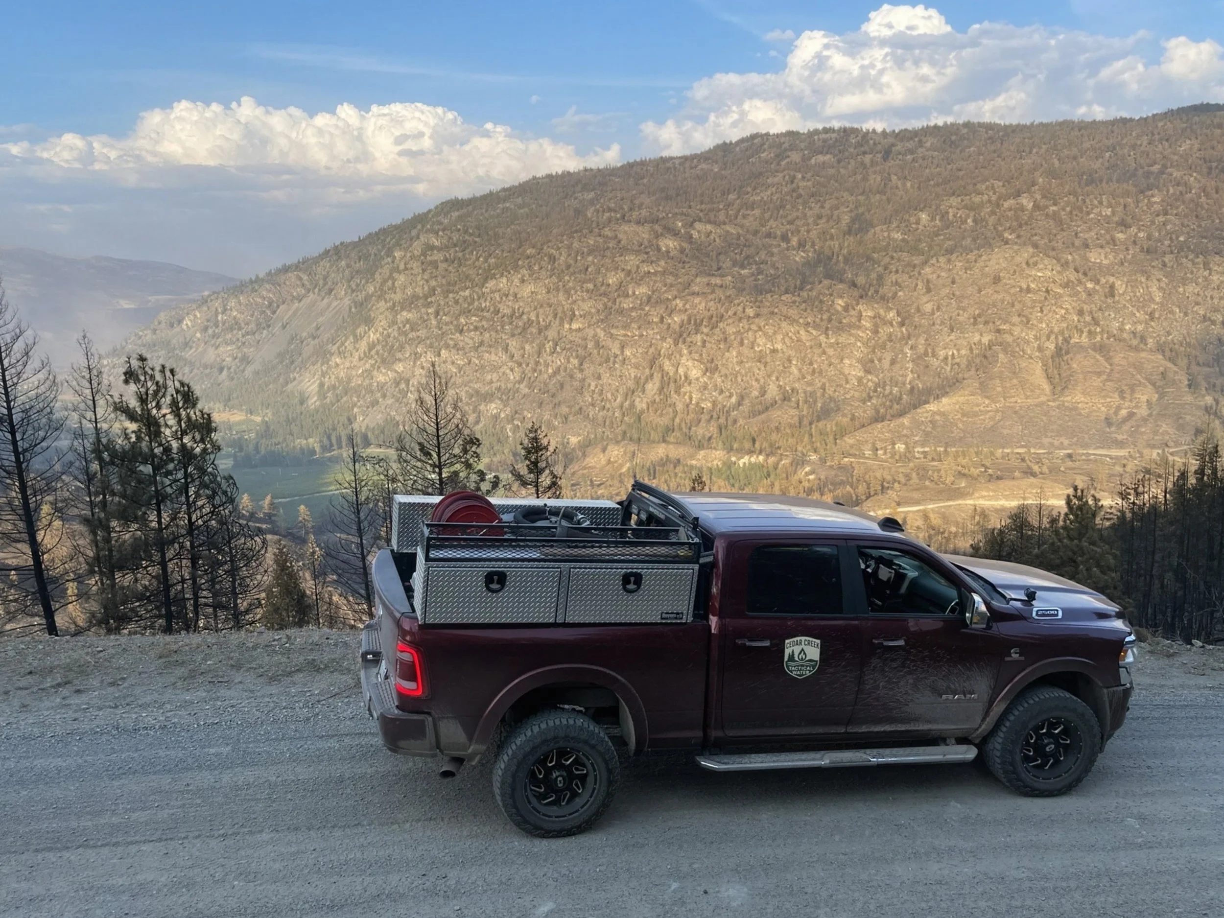 Maroon Ram 2500 work truck with equipment rack parked on a mountain road overlooking a forested canyon