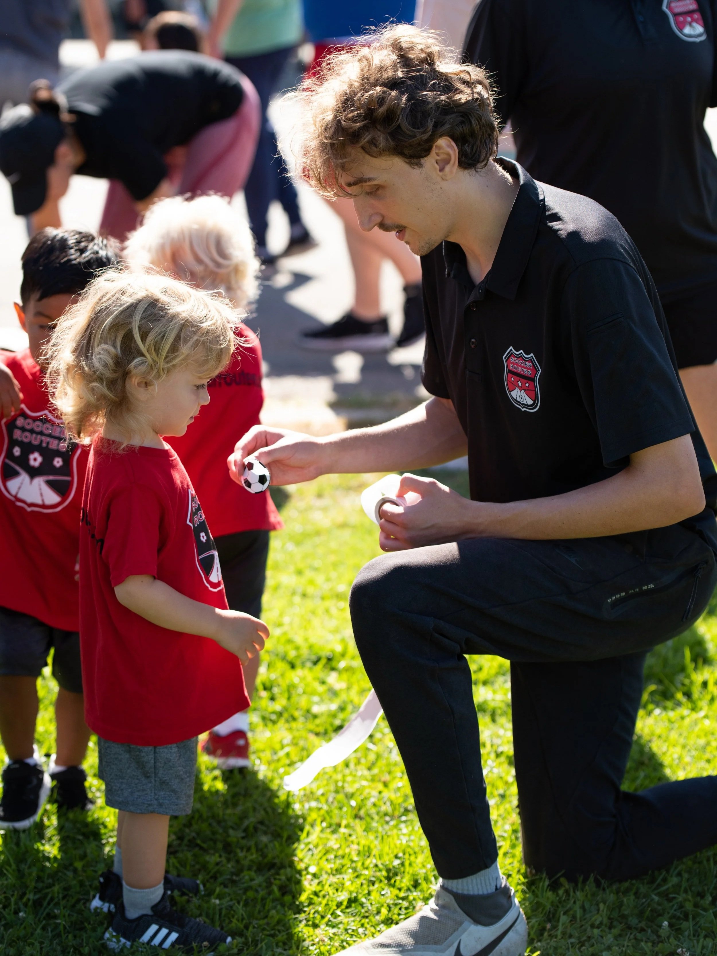 Soccer coach handing a child a soccer ball at an outdoor youth practice