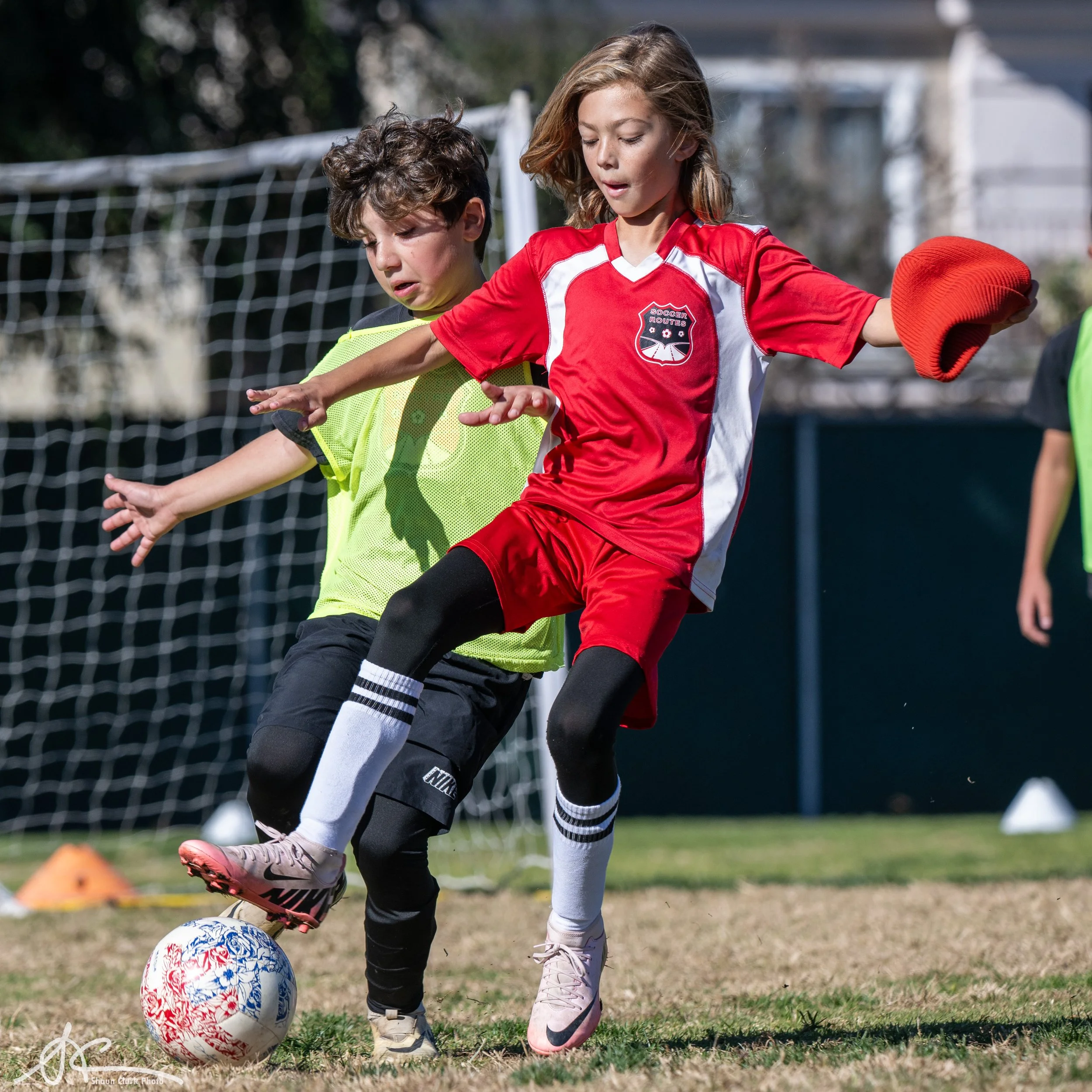 Youth soccer players compete for the ball in front of a goal during an outdoor game.