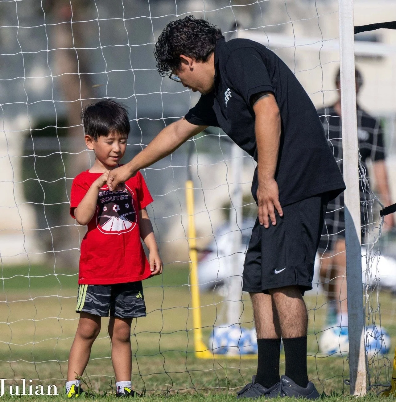 Soccer coach fist-bumping a young boy in front of a goal net on a grassy field