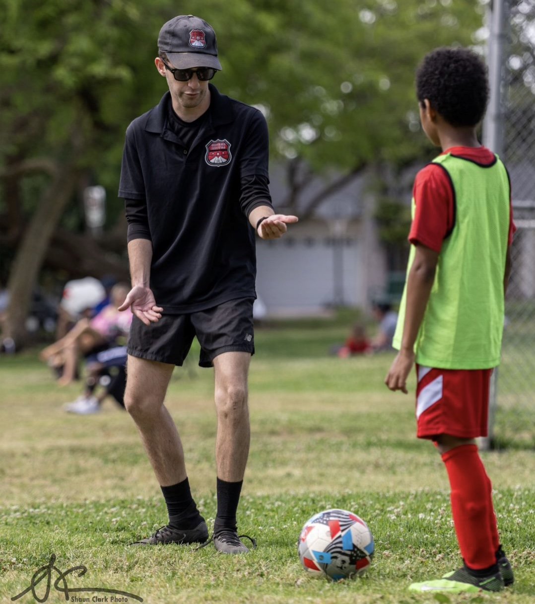 Soccer coach instructing a young player on a grassy field beside a soccer ball