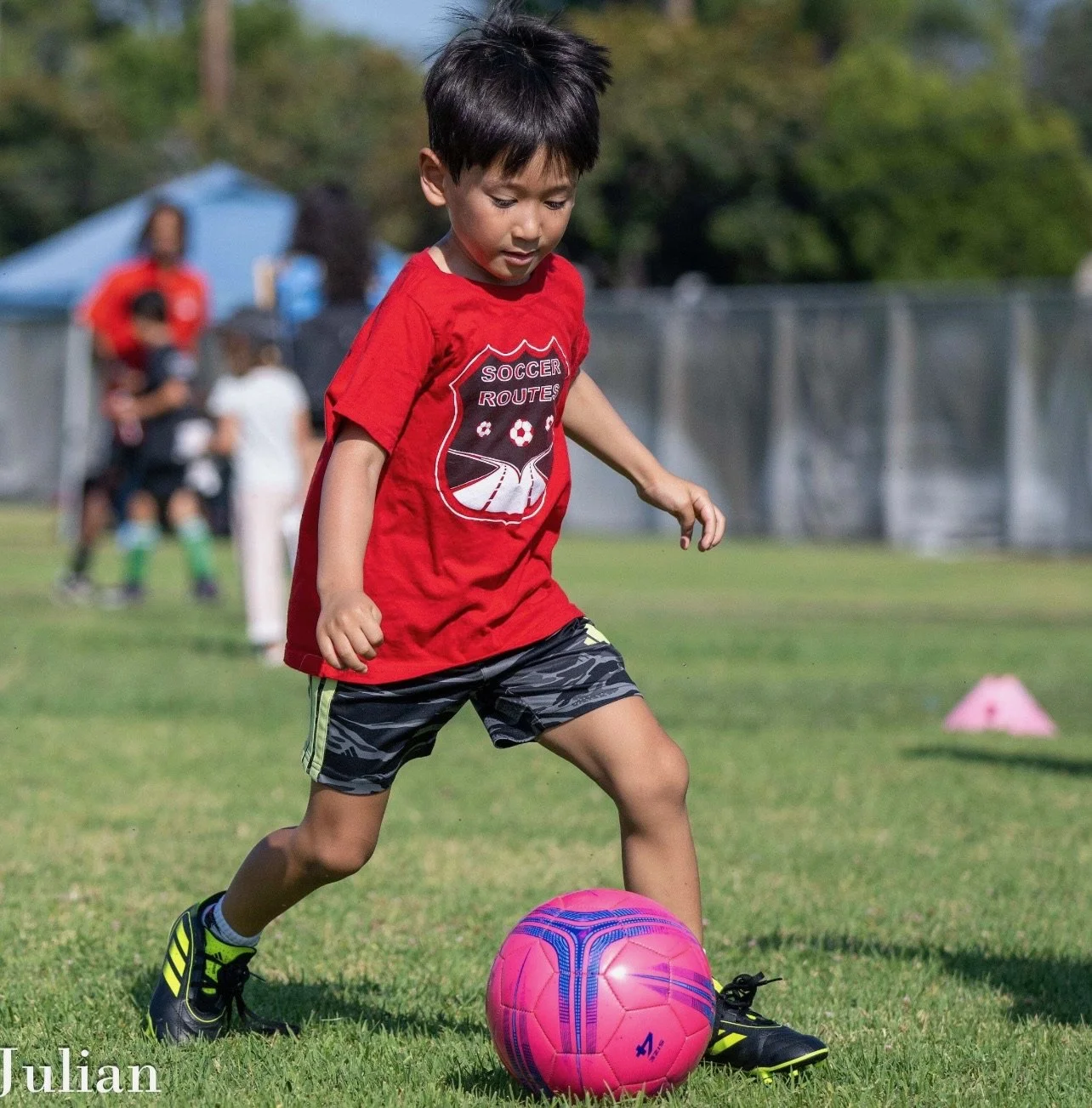 Young boy in a red soccer shirt dribbling a pink soccer ball on a grassy field