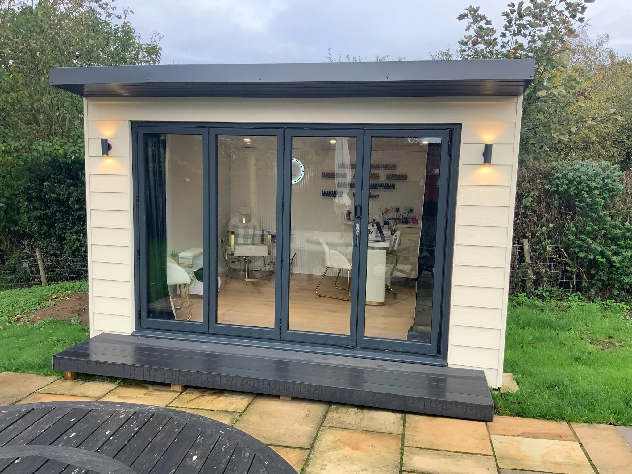 Modern backyard beauty salon garden studio with glass folding doors, manicure stations, and black deck