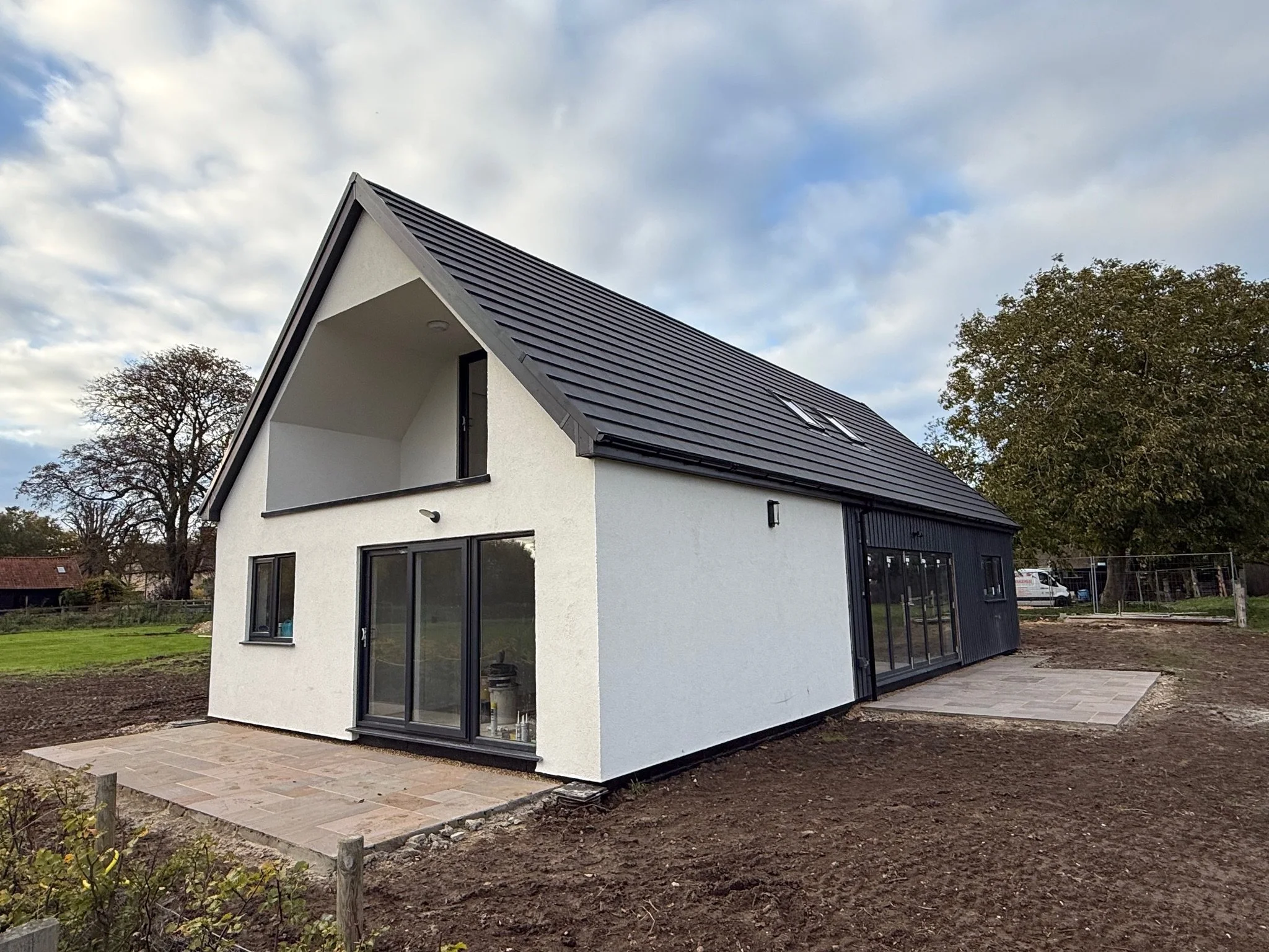 Modern white house with a steep dark tiled roof, skylight, black-framed windows, patio, and landscaped yard