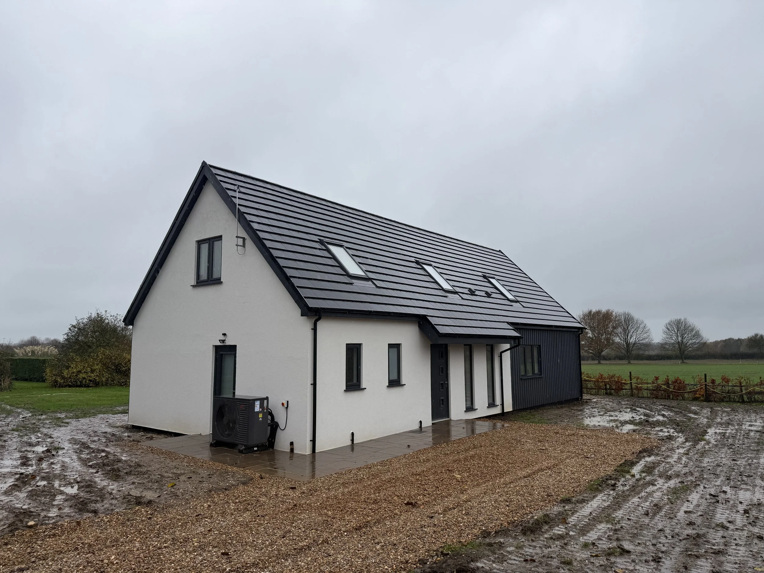 Modern white rural house with a dark tiled roof, skylights, heat pump