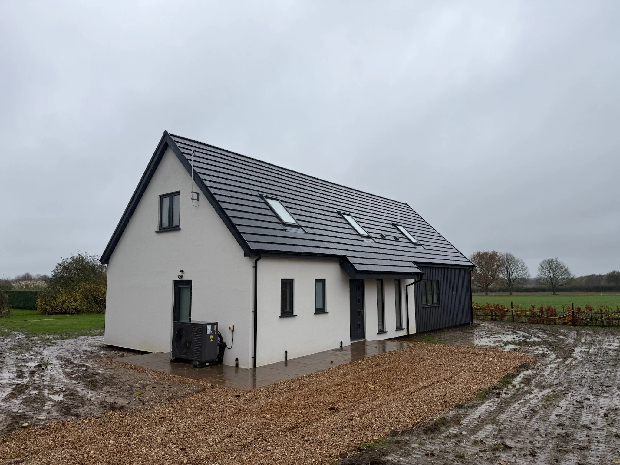Modern white rural house with dark tiled roof, skylights