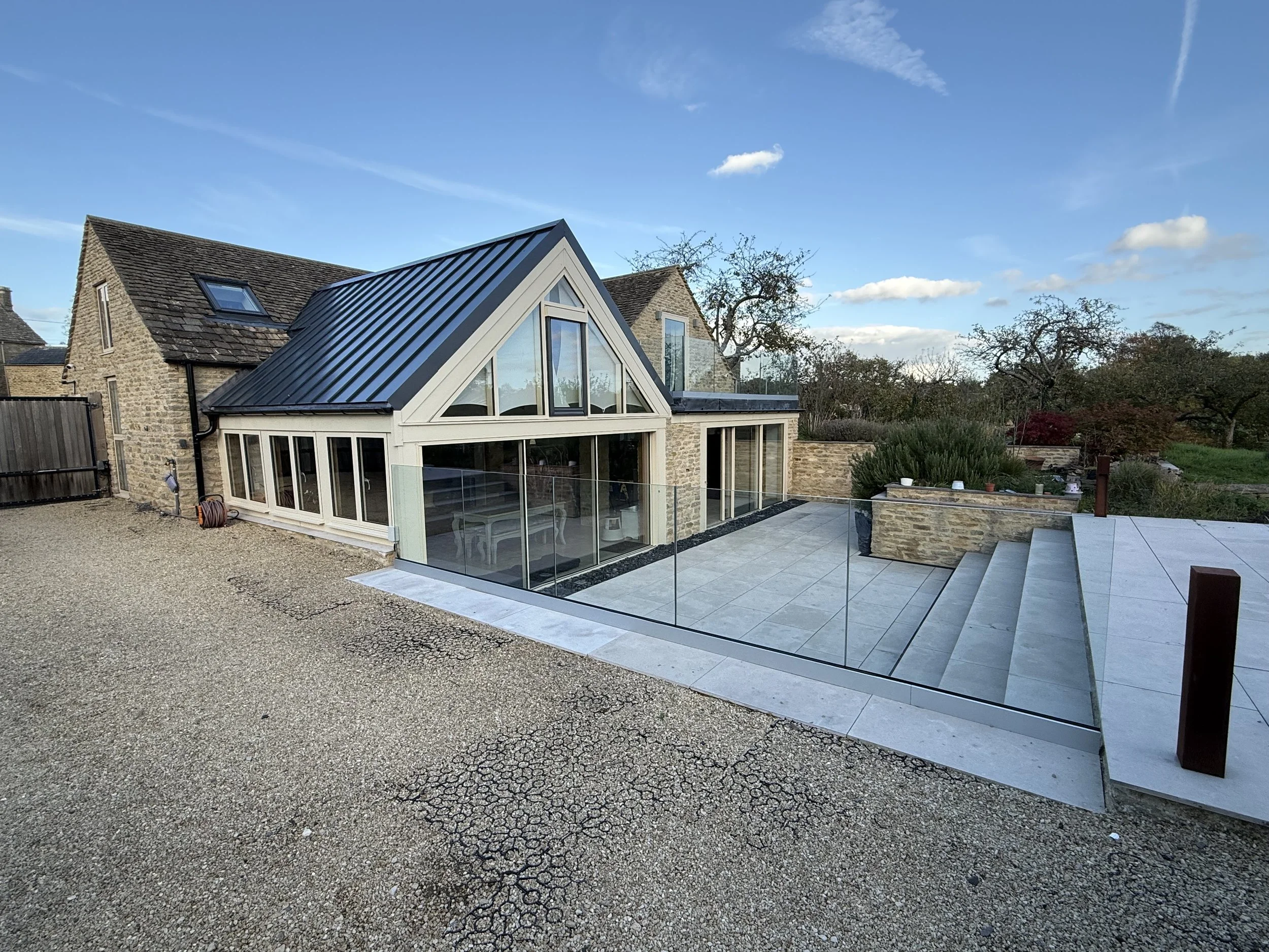 Stone cottage with modern glass extension, landscaped patio, and gravel driveway