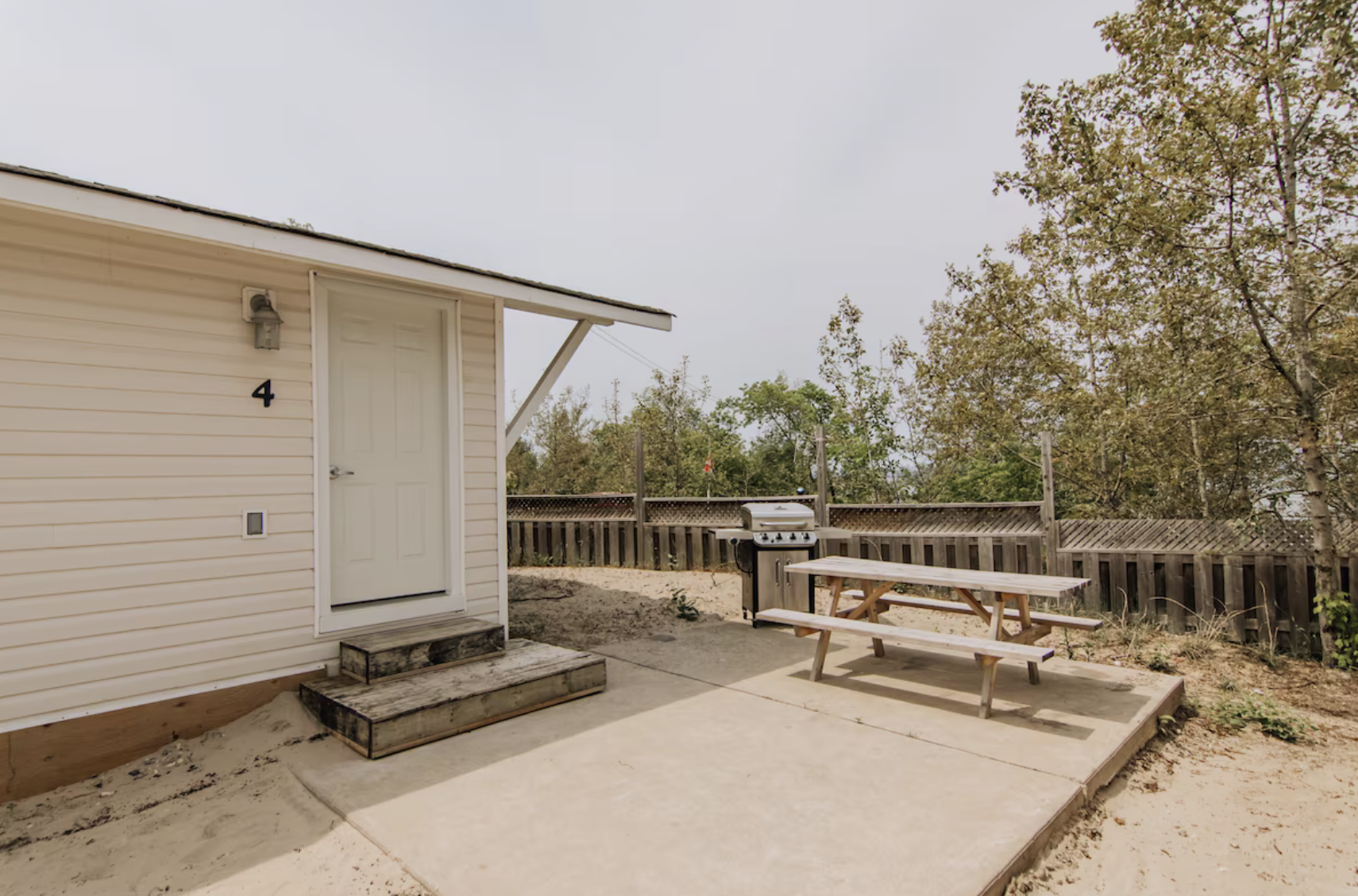 Outdoor patio beside a small building with a door labeled 4, picnic table, gas grill, and wooded surroundings