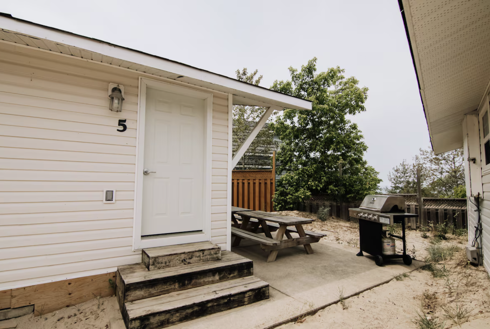 Outdoor patio beside a white building with door number 5, picnic table, and gas grill