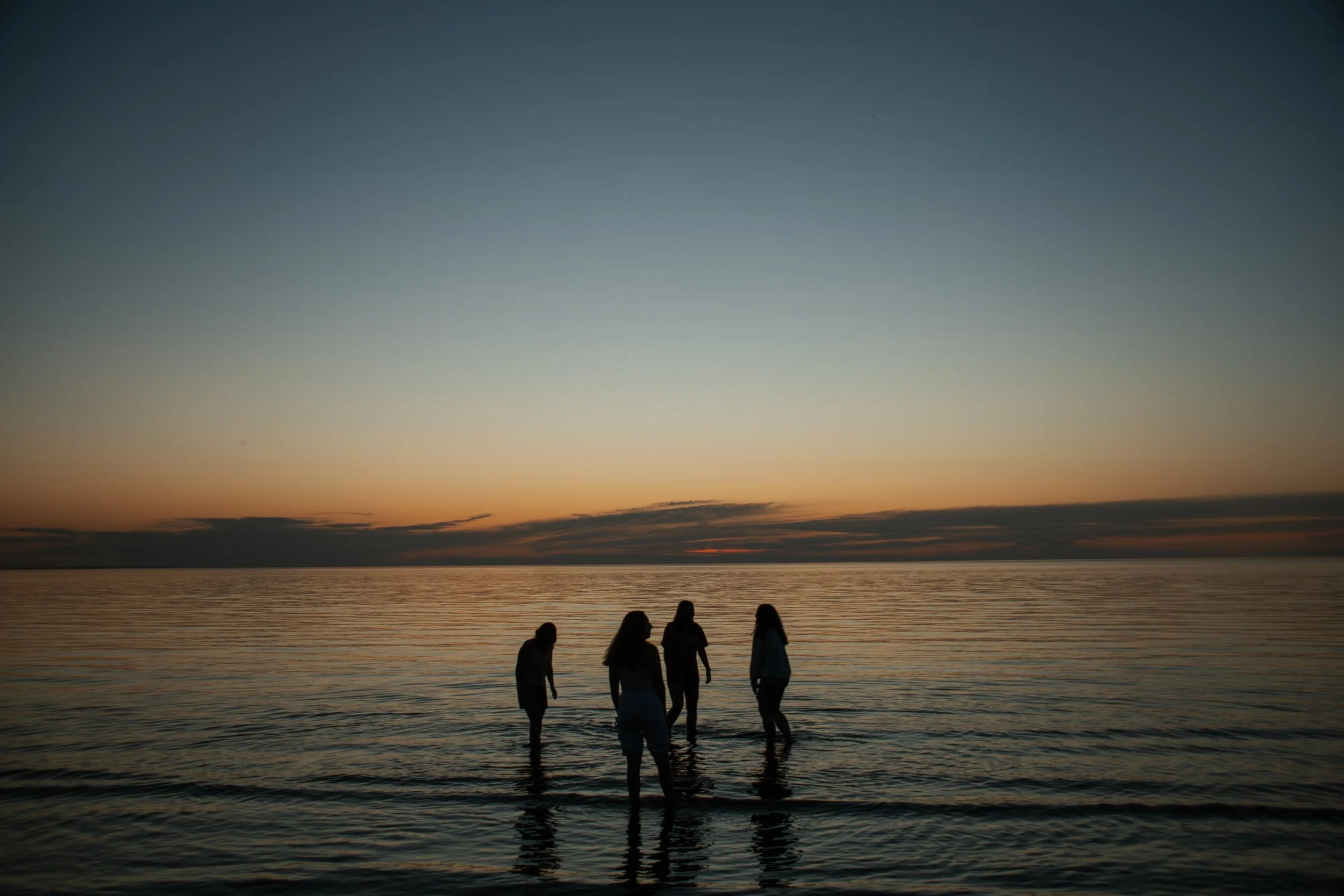 Silhouettes of four people wading in calm water at sunset