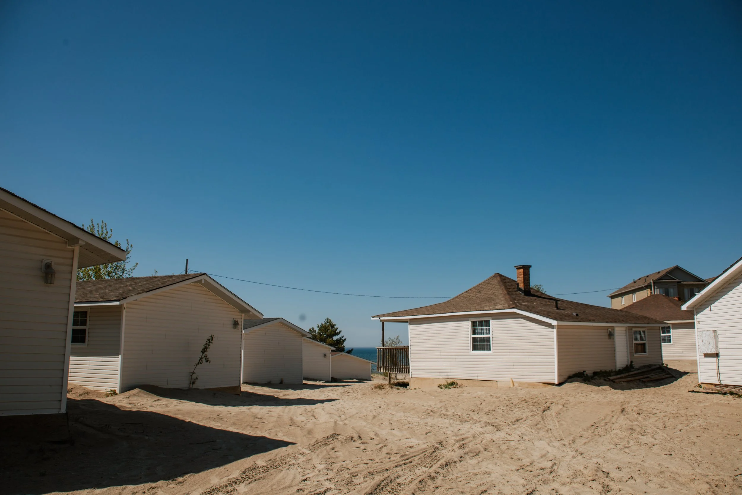White-sided homes on sandy ground under a clear blue sky, with a glimpse of water in the distance