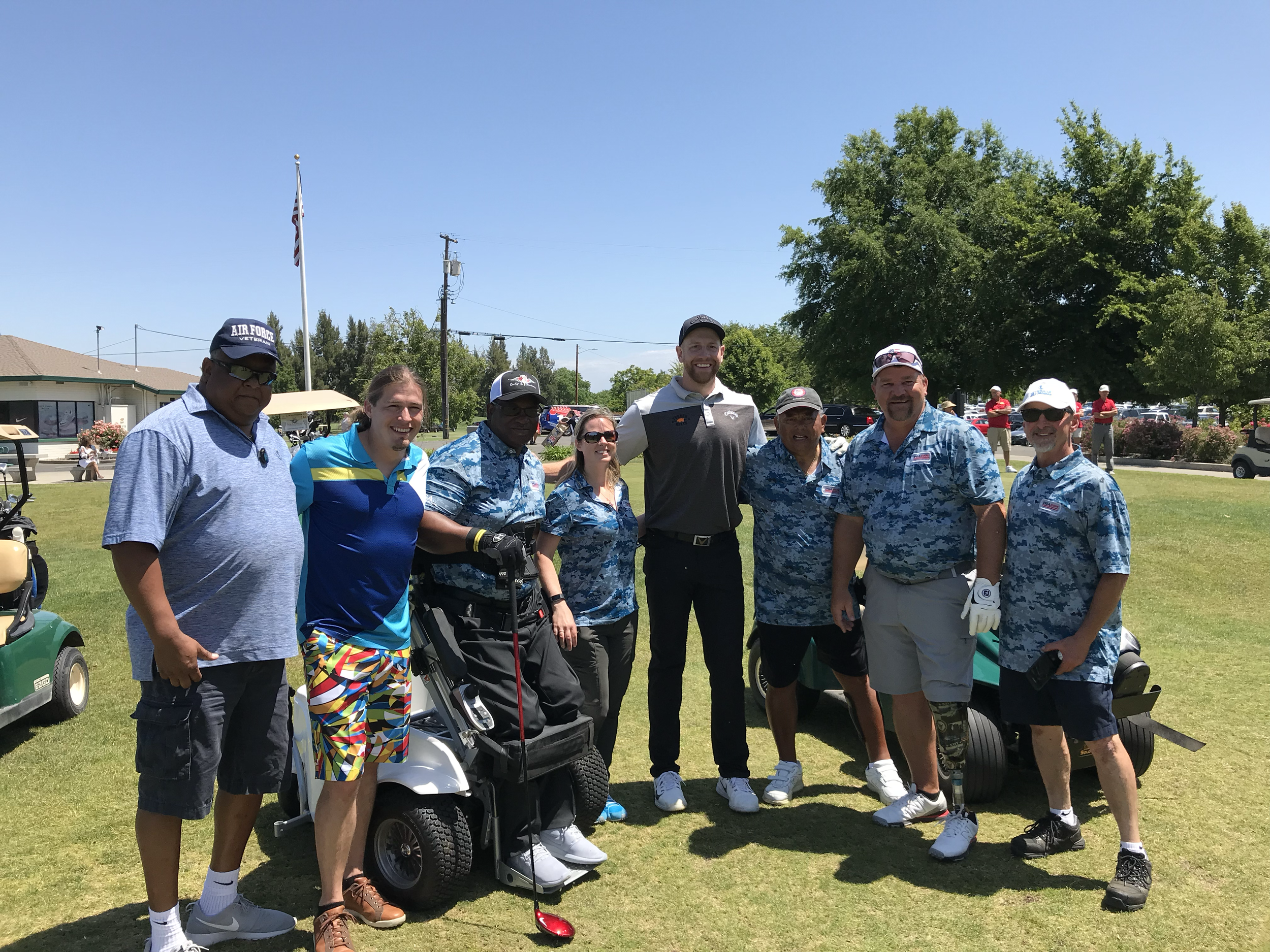 Group of golfers posing on a sunny golf course beside golf carts and an American flag