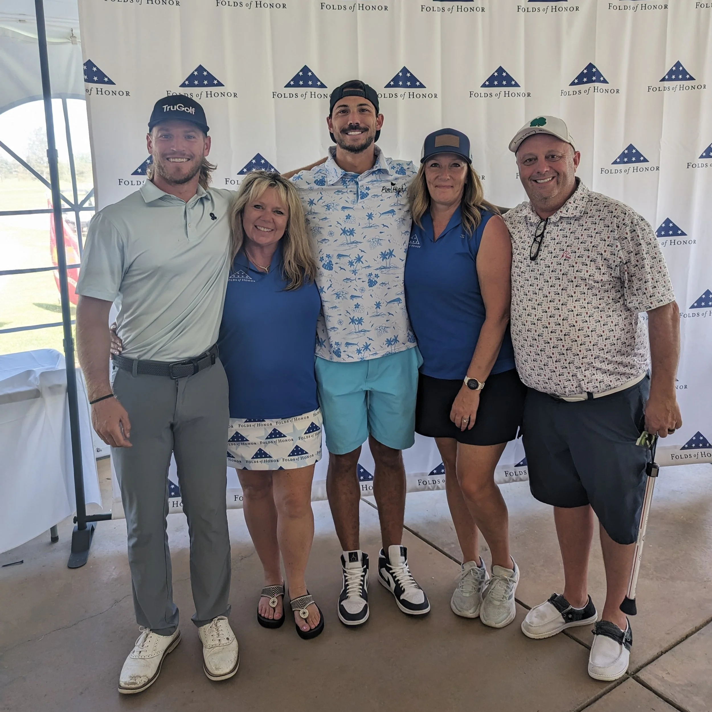 Group of five people posing at a golf event in front of a Folds of Honor backdrop.