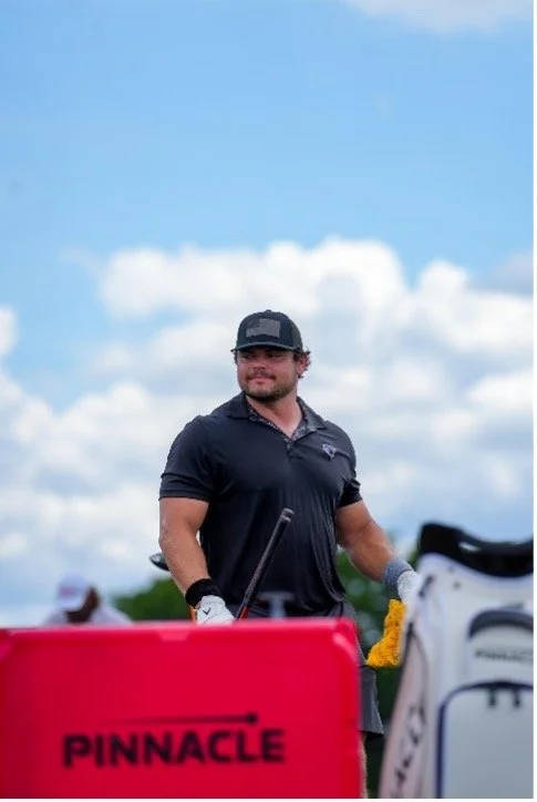 Golfer standing beside a red Pinnacle golf ball cooler and golf bag under a blue sky