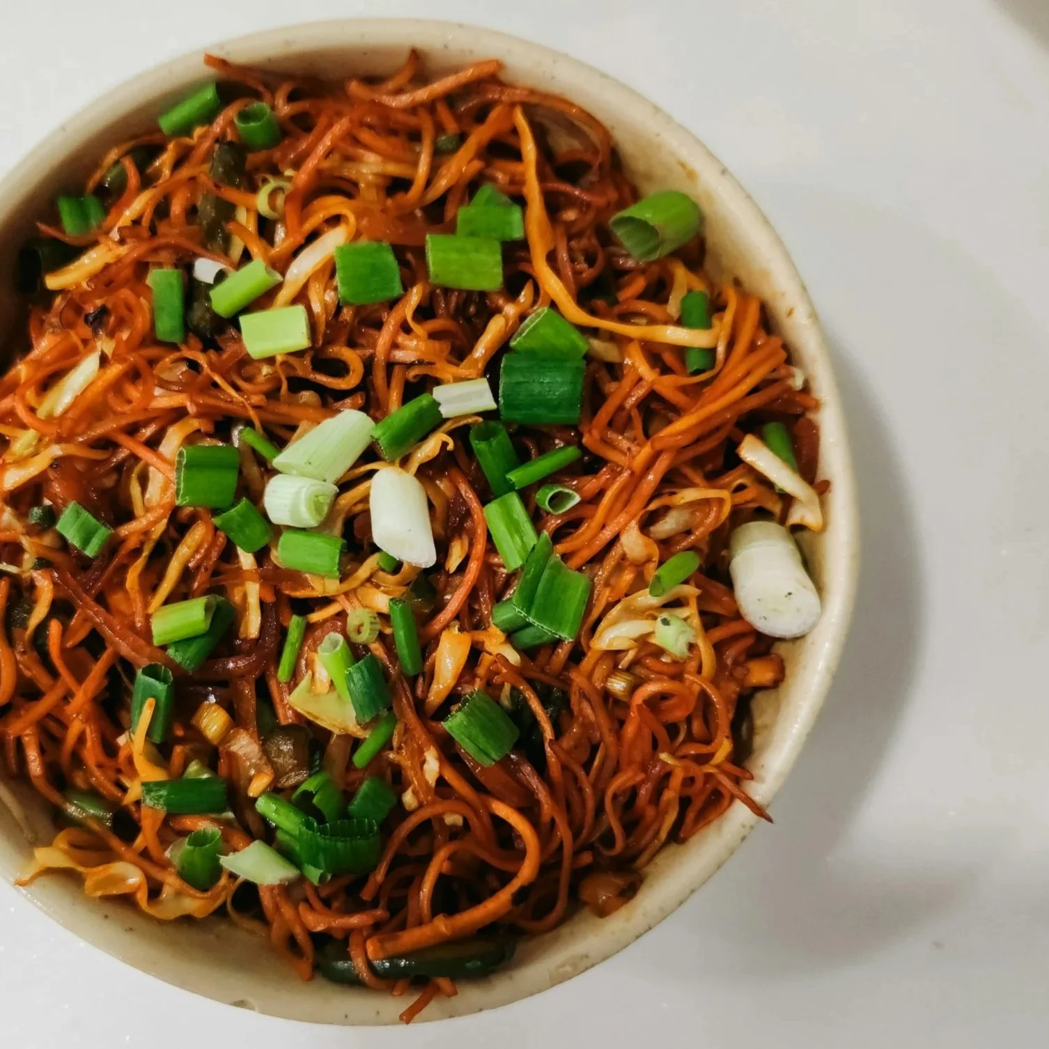 Spicy stir-fried noodles with vegetables and chopped green onions in a bowl
