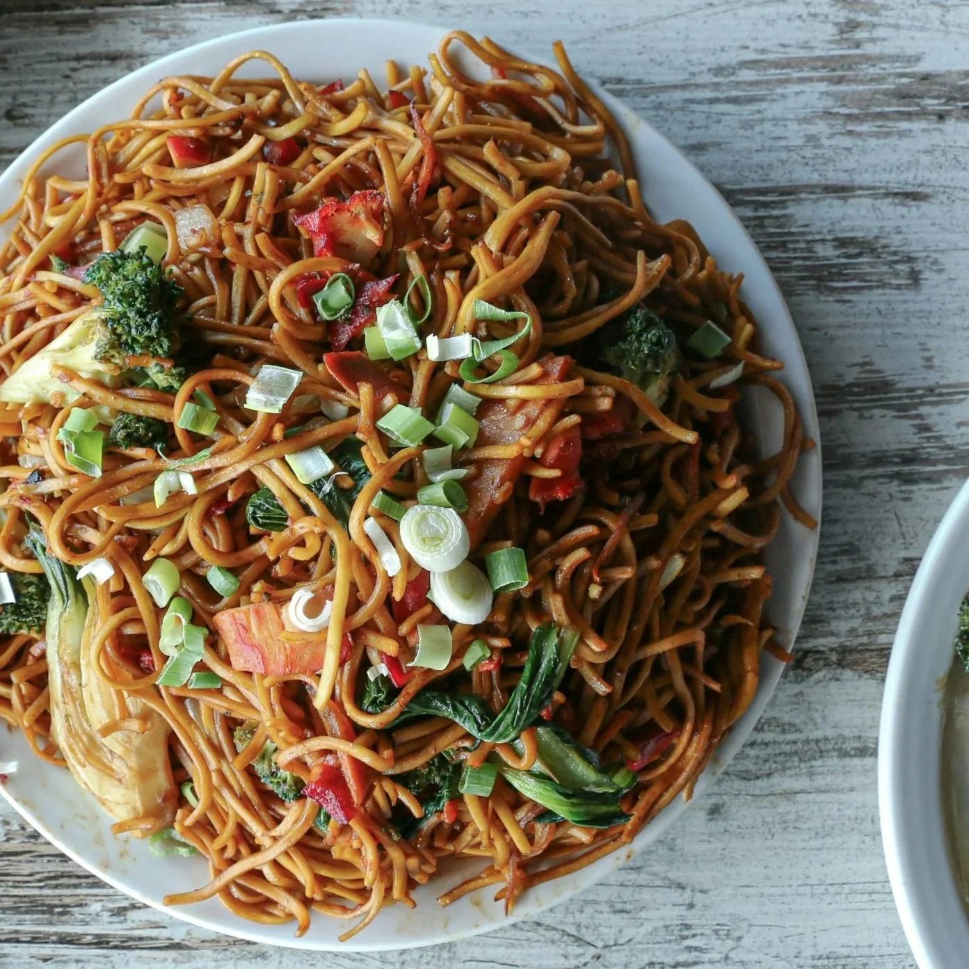 Vegetable chow mein noodles with broccoli, bell peppers, bok choy, and green onions on a white plate