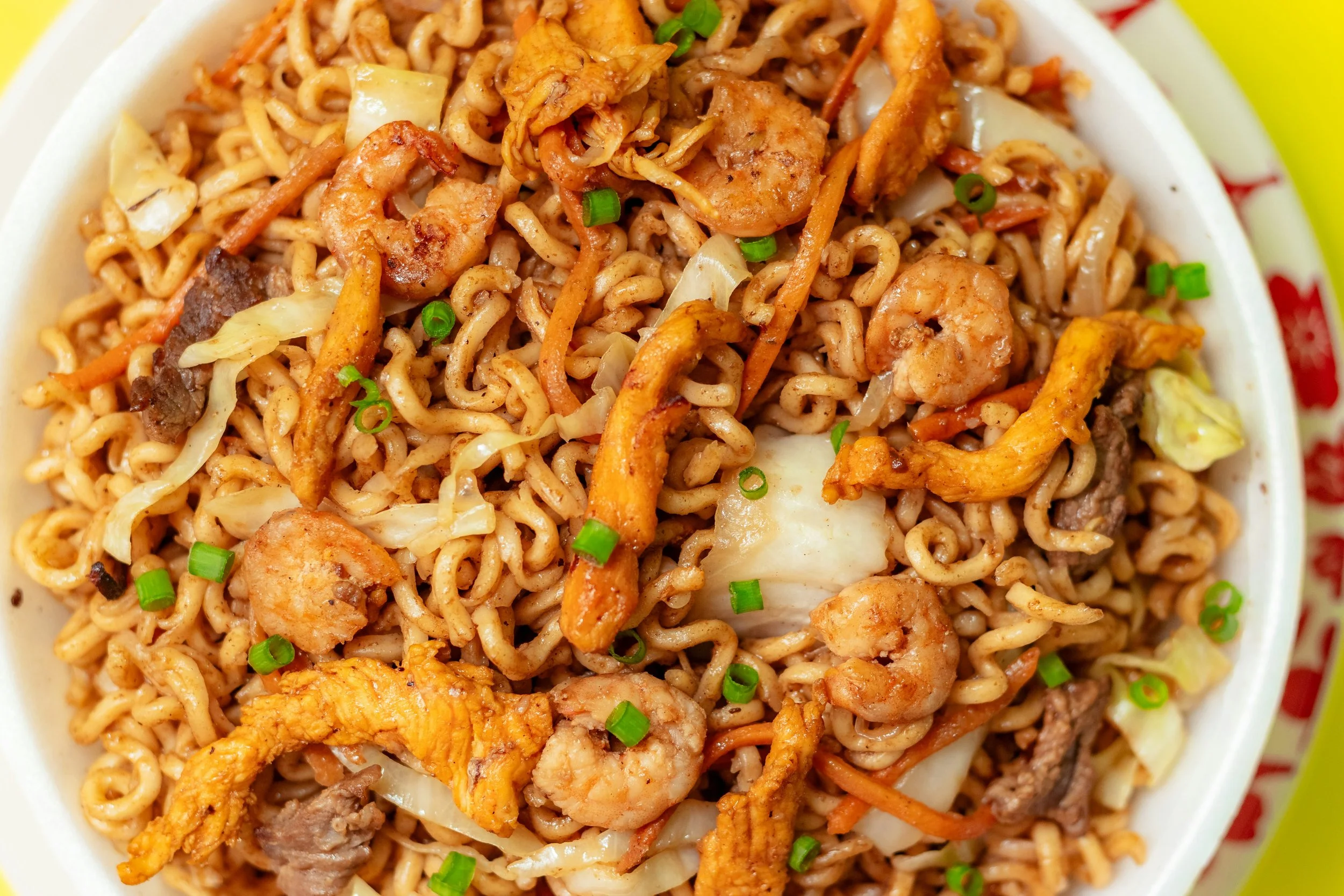 Close-up of stir-fried noodles with shrimp, chicken, beef, carrots, cabbage, and green onions