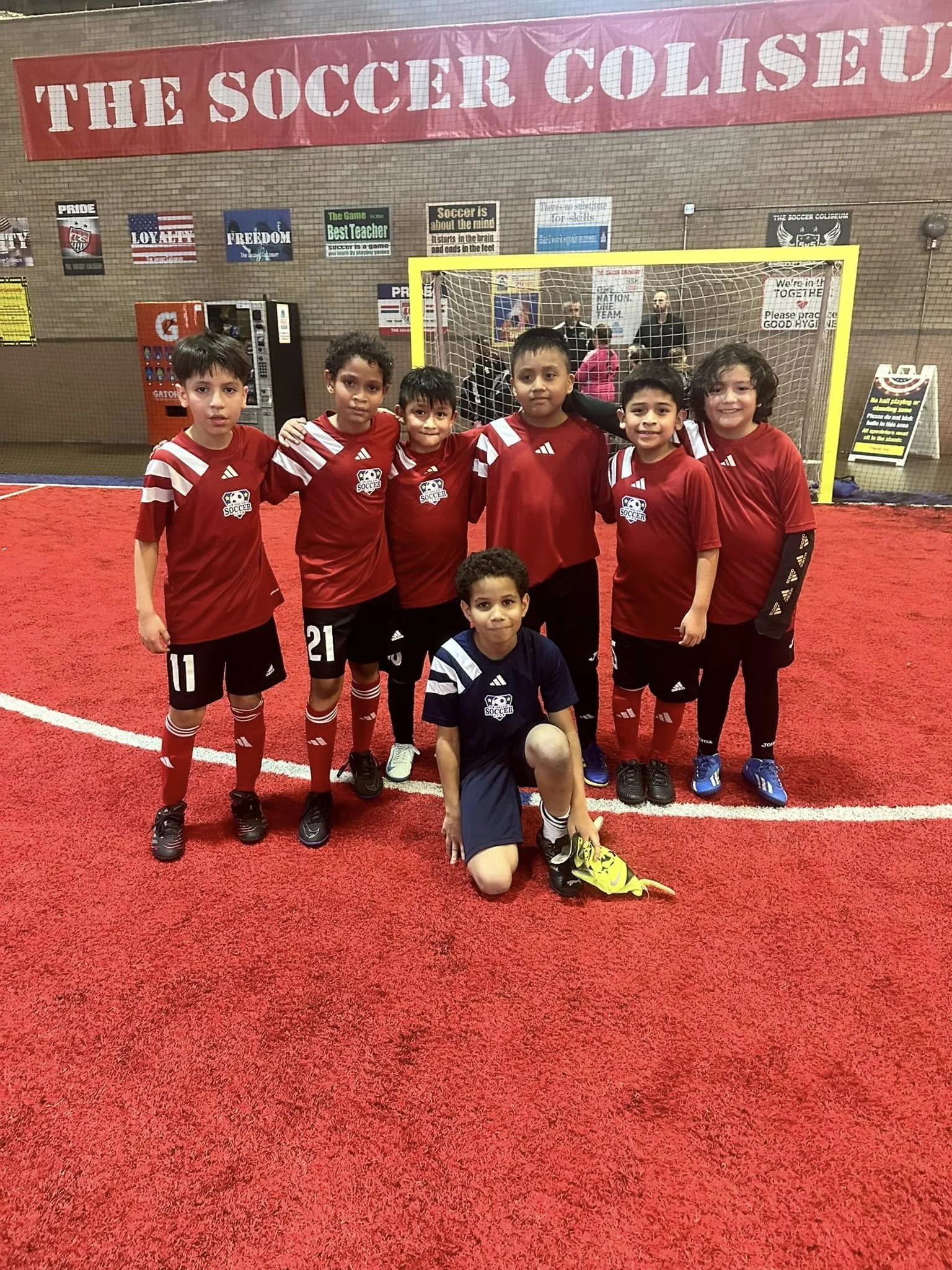Youth soccer team posing in red uniforms on an indoor soccer field in front of a goal.