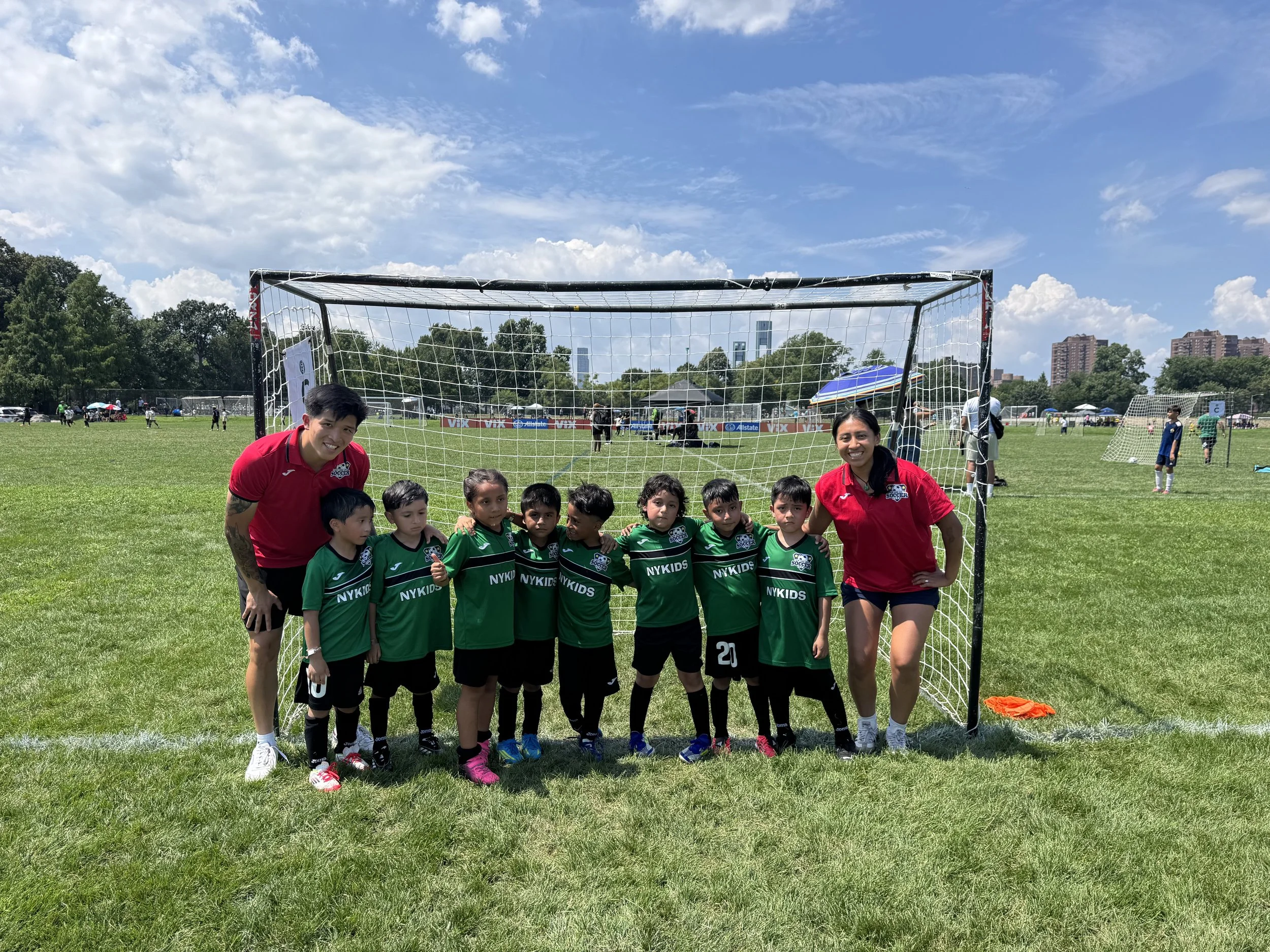 Youth soccer team posing with two coaches in front of a goal on a sunny outdoor field.