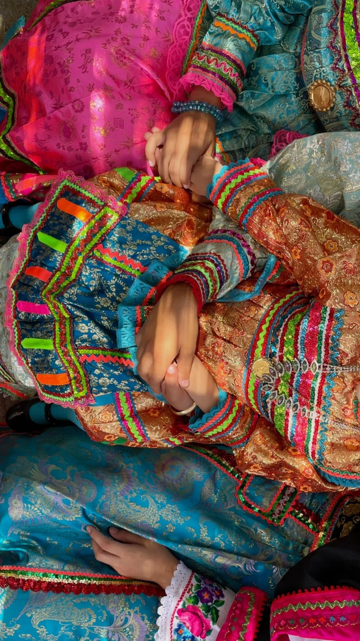 Close-up of people wearing vibrant embroidered traditional clothing with colorful trim, ornate patterns, and decorative bracelets.