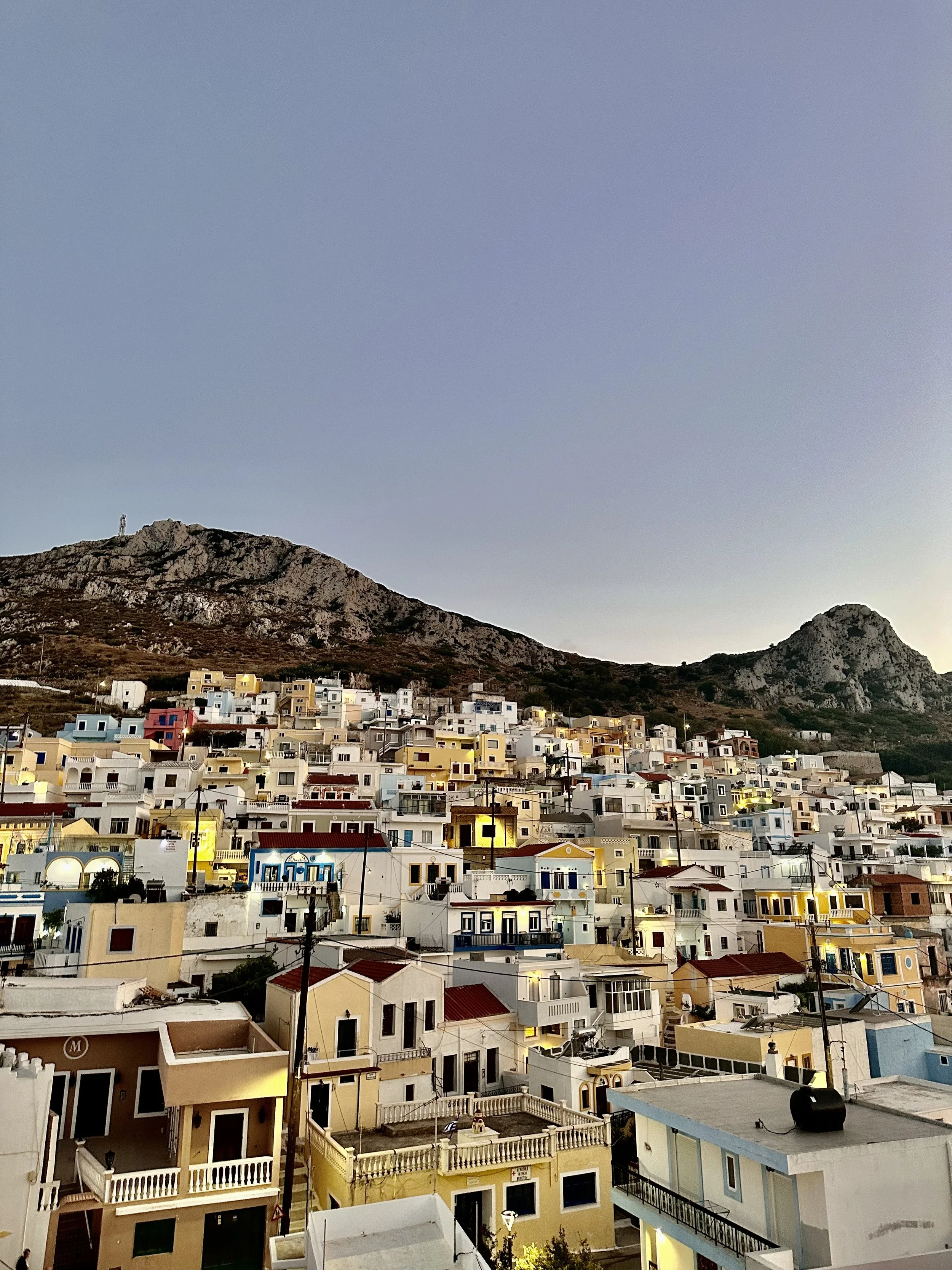 Colorful hillside village beneath rugged rocky mountains at dusk