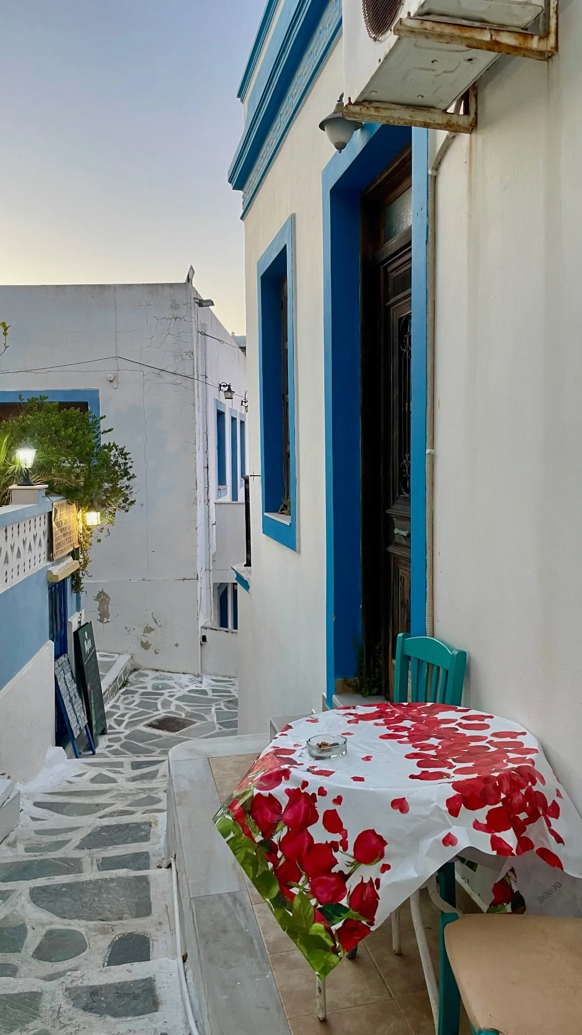 Blue-and-white Mediterranean courtyard with a rose-covered table, turquoise chair, stone walkway, and traditional doorway