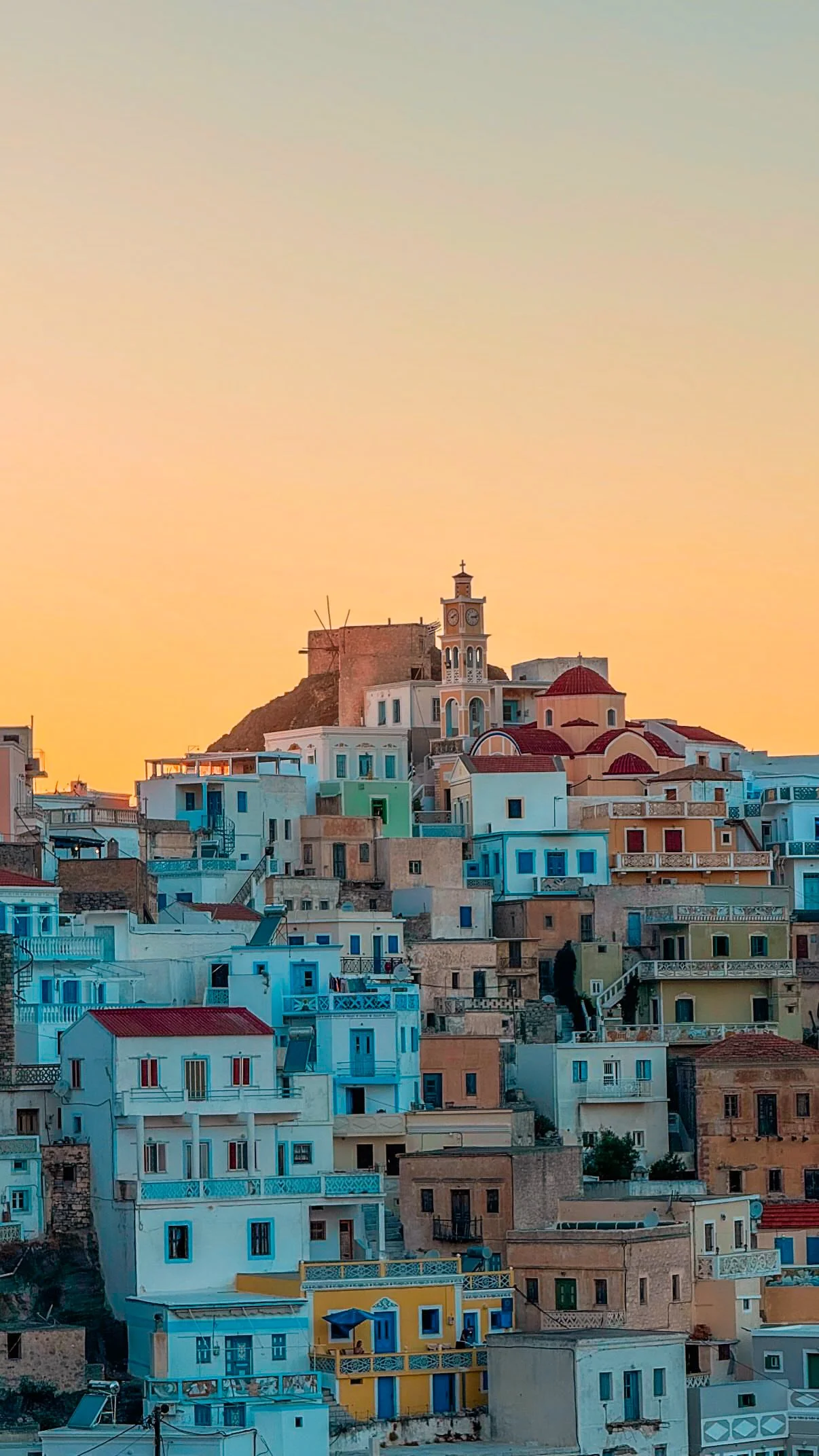 Colorful hillside village with turquoise and pastel homes, a clock tower, and church dome at sunset