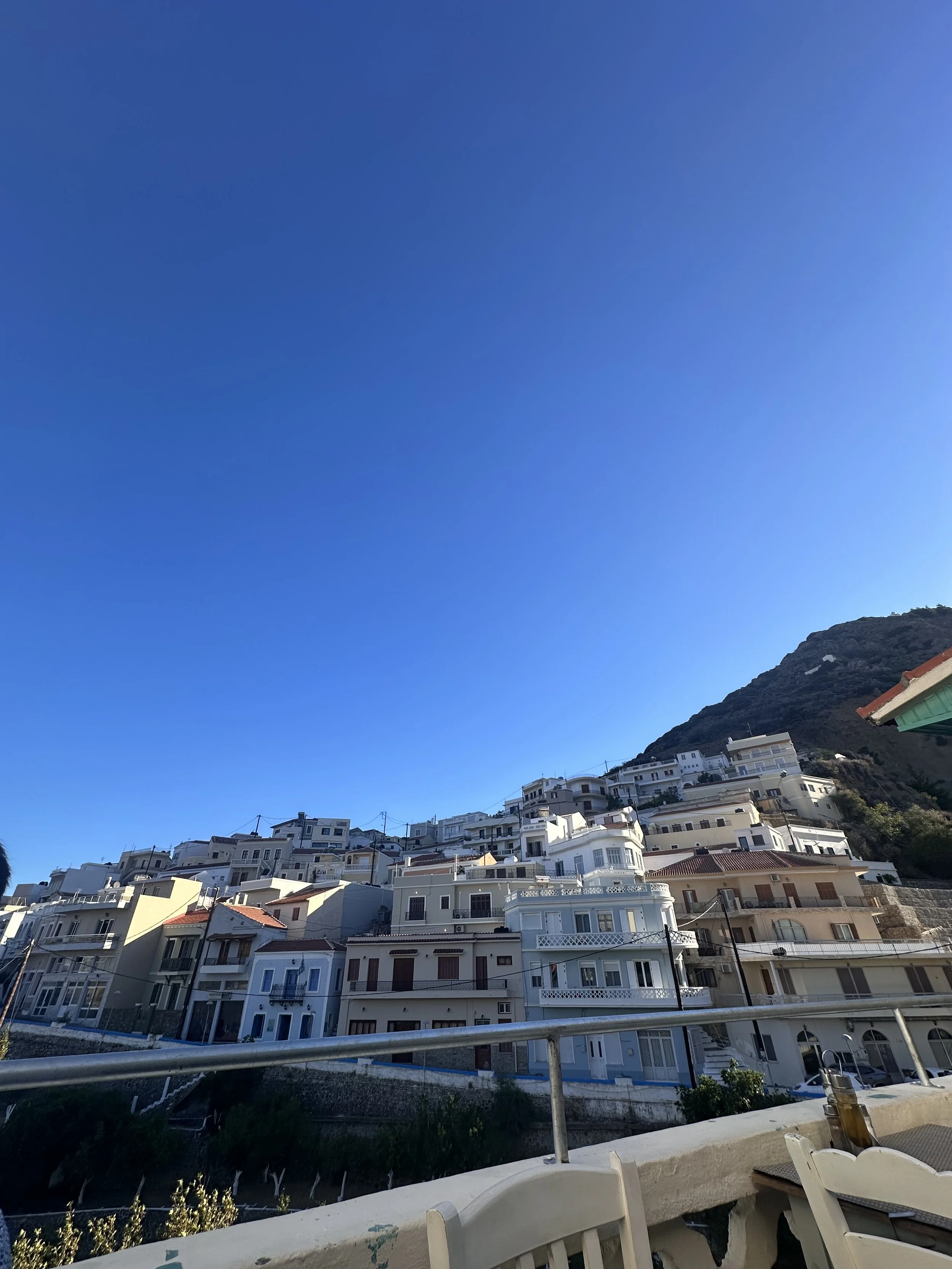 Whitewashed hillside village with balconies beneath a rugged mountain and clear blue sky