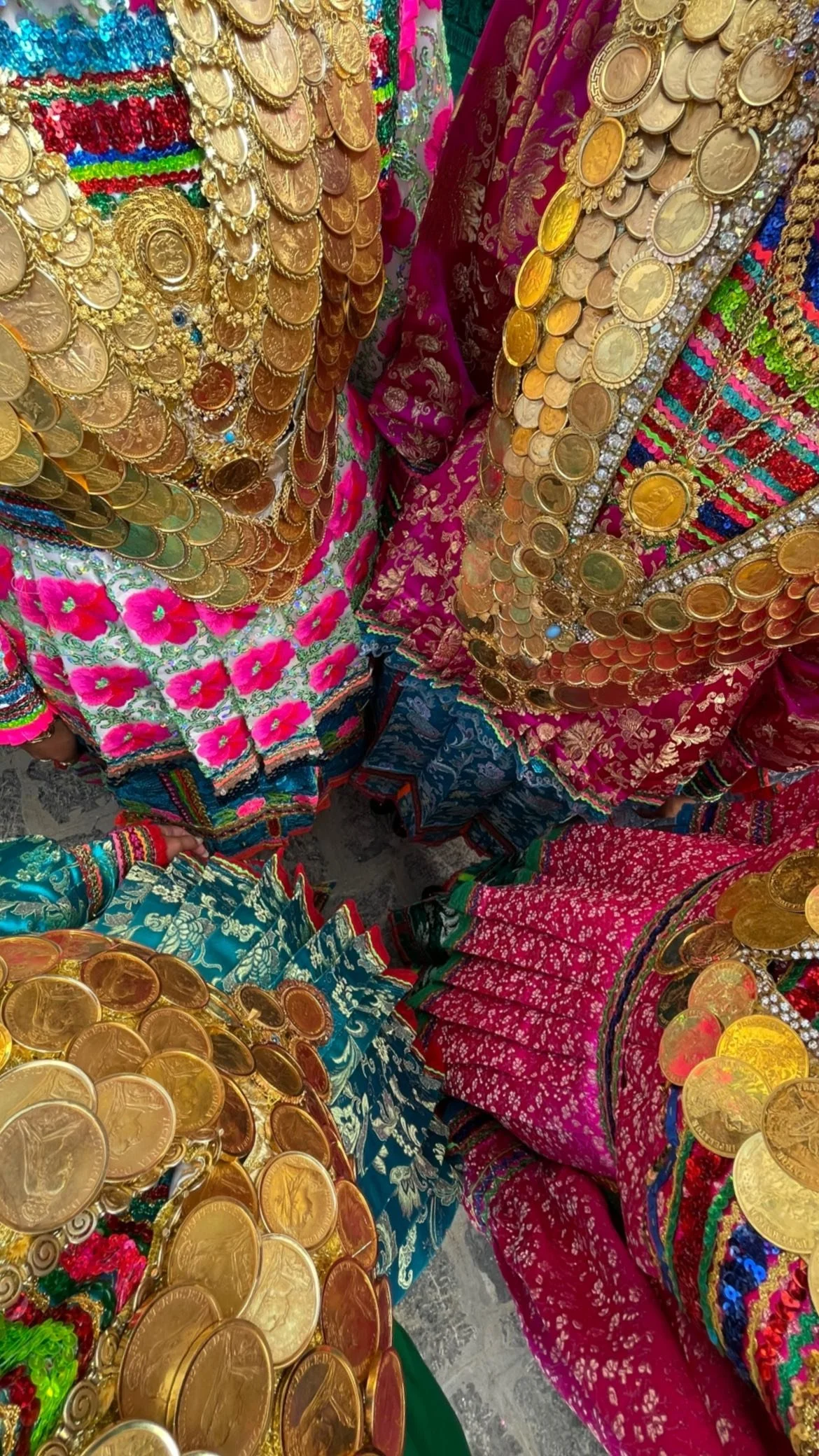 Colorful traditional garments richly decorated with layered gold coin embellishments and intricate embroidered patterns