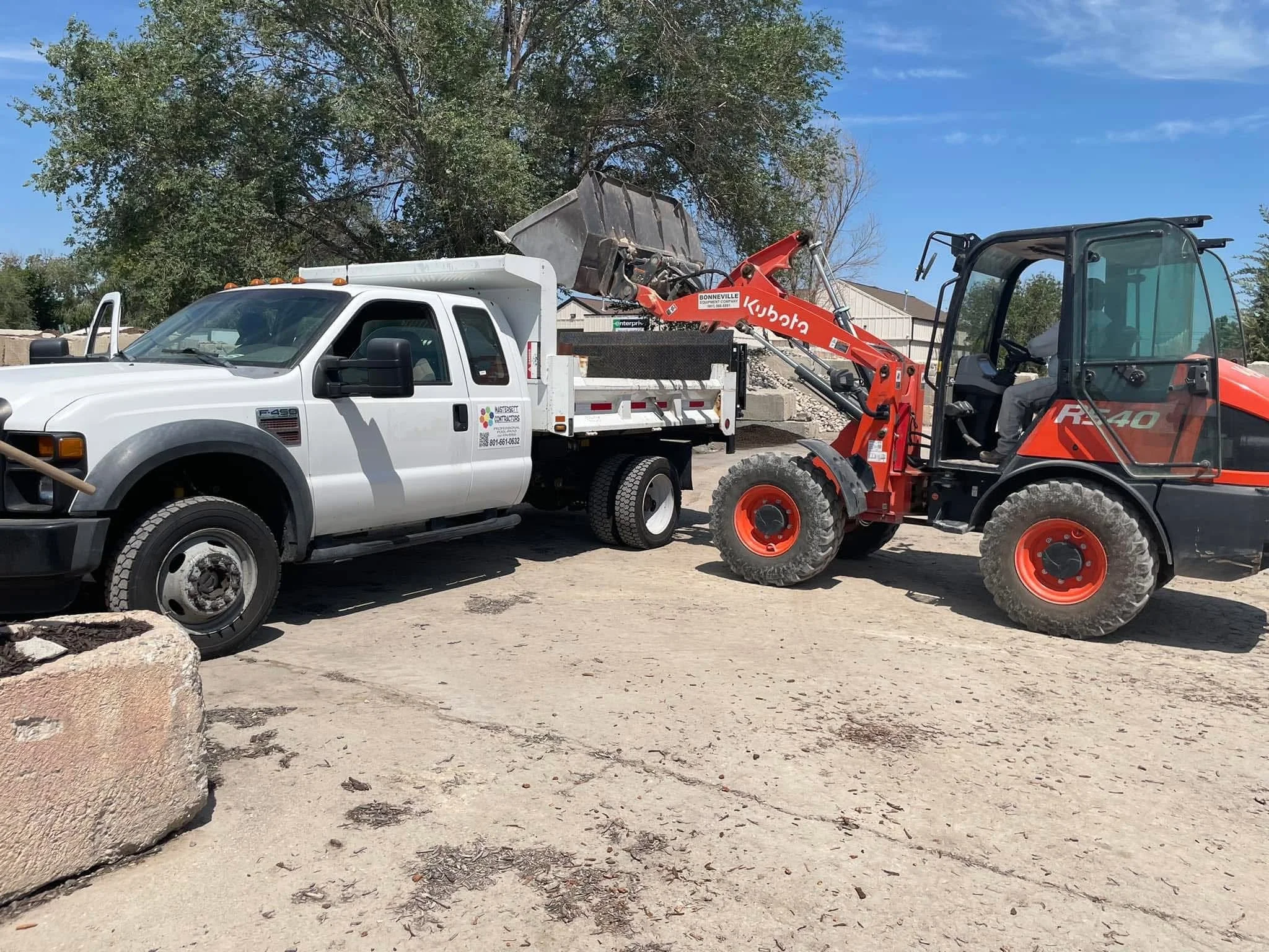 Kubota wheel loader loading gravel into a white dump truck at a landscaping supply yard.
