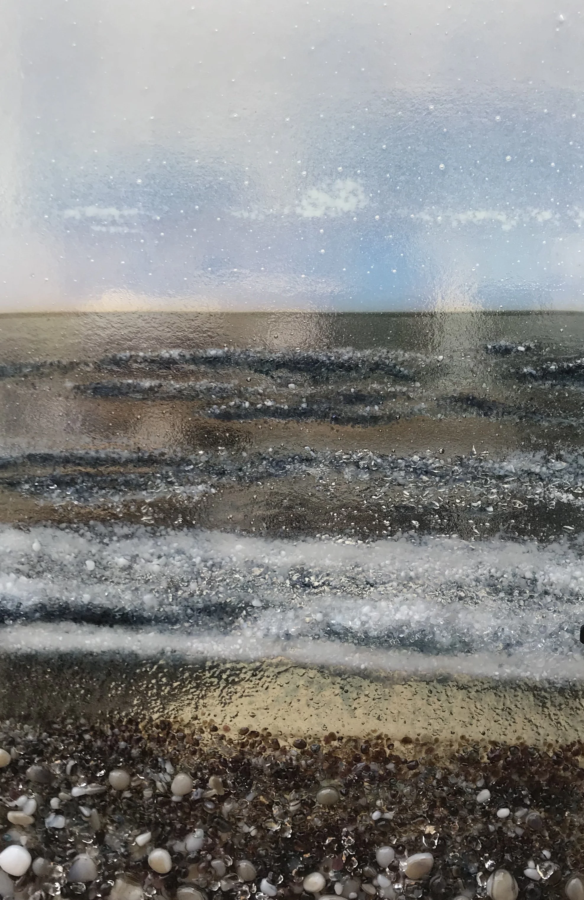 Close-up of a textured ocean wave with white foam, viewed through a water-speckled window