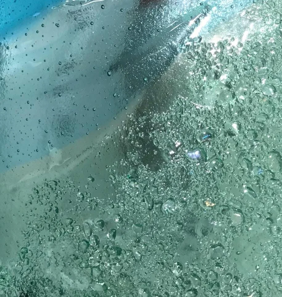 Close-up of water droplets and bubbles on translucent blue-green glass