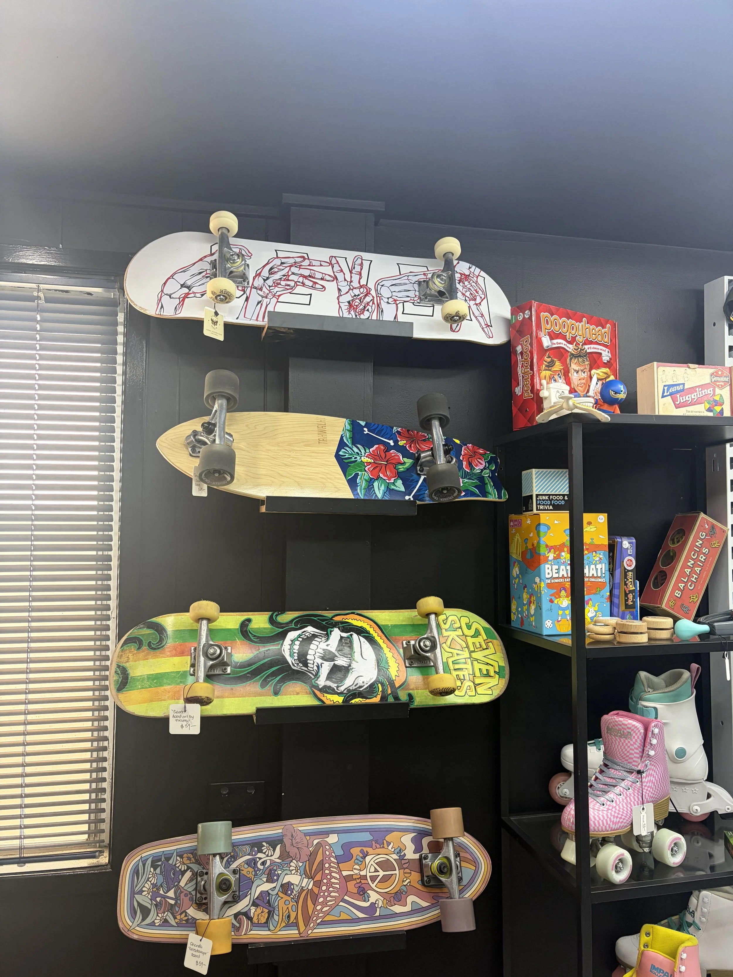 Colorful skateboards displayed on a black wall beside board games and roller skates in a shop.