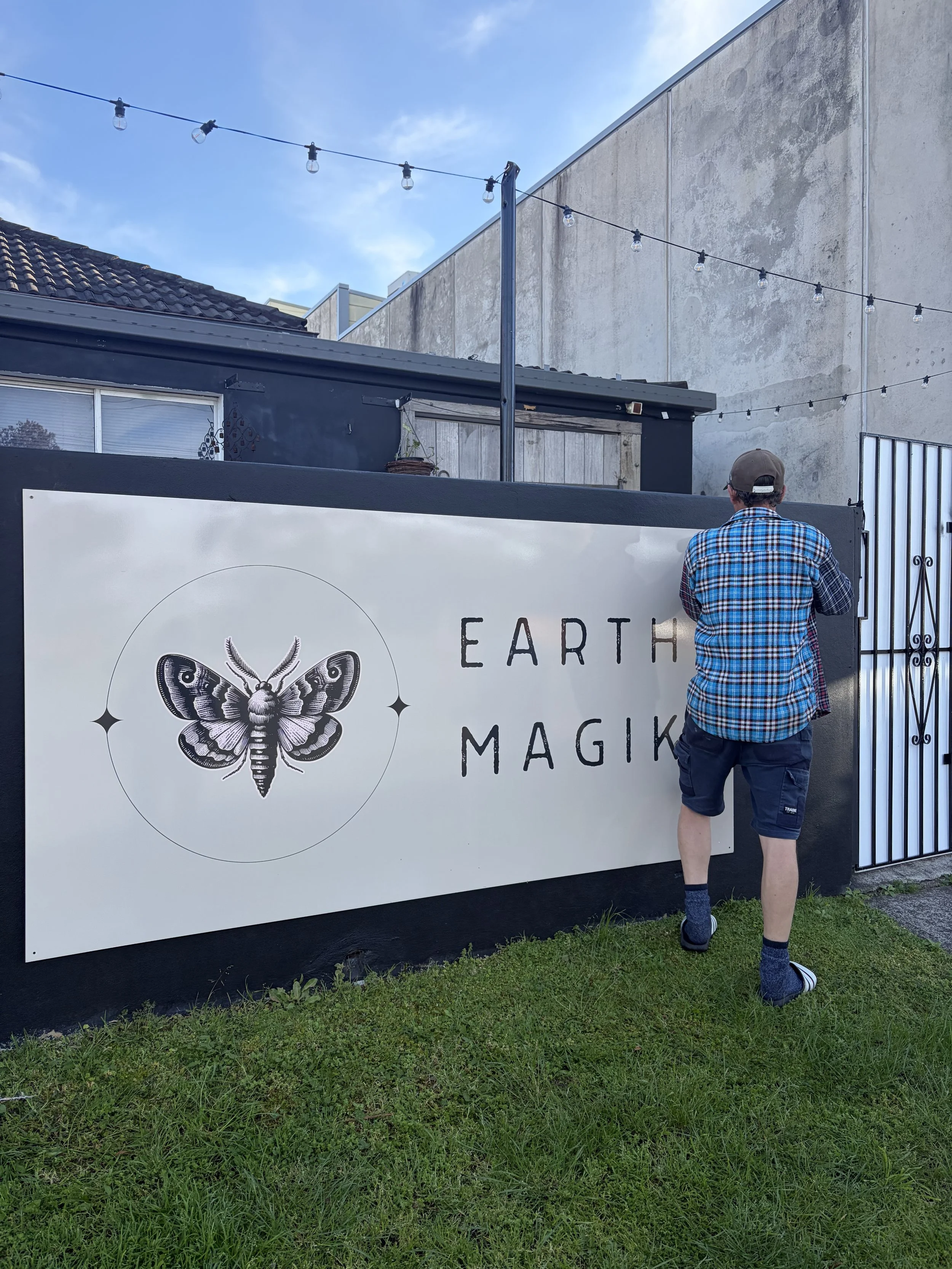 Person standing beside an Earth Magic moth mural beneath outdoor string lights.
