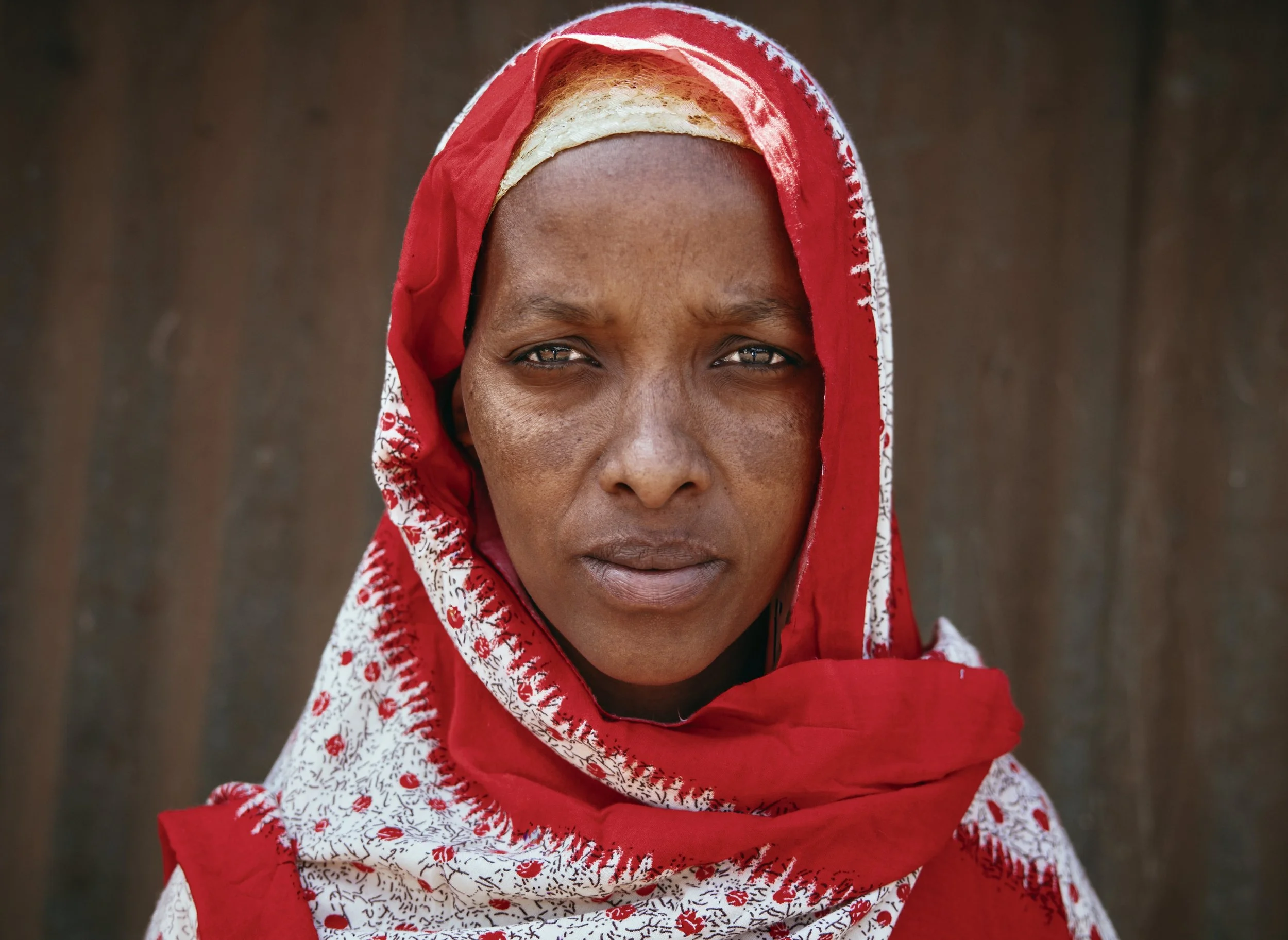 Close-up portrait of a woman wearing a red-and-white patterned headscarf against a brown background in Kenya. Photo by David Ferry Jr.